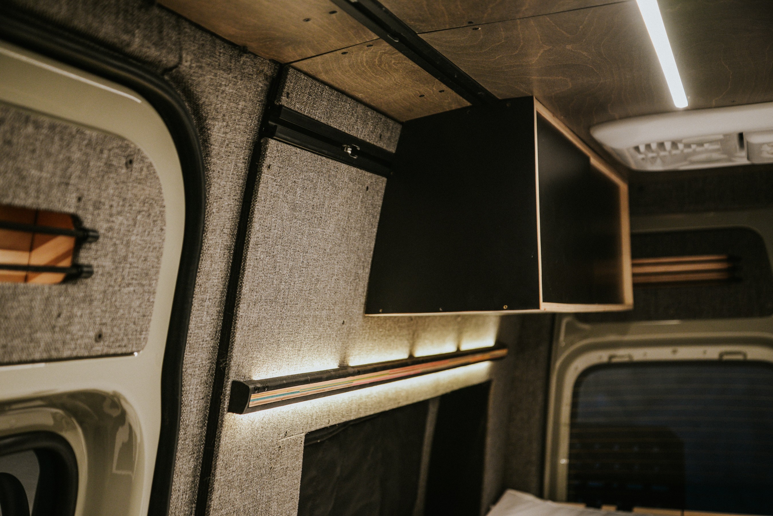 Modern RV rental interior showing textured fabric walls, wooden ceiling, overhead storage, and integrated LED lighting.. Mercedes Sprinter 2021
