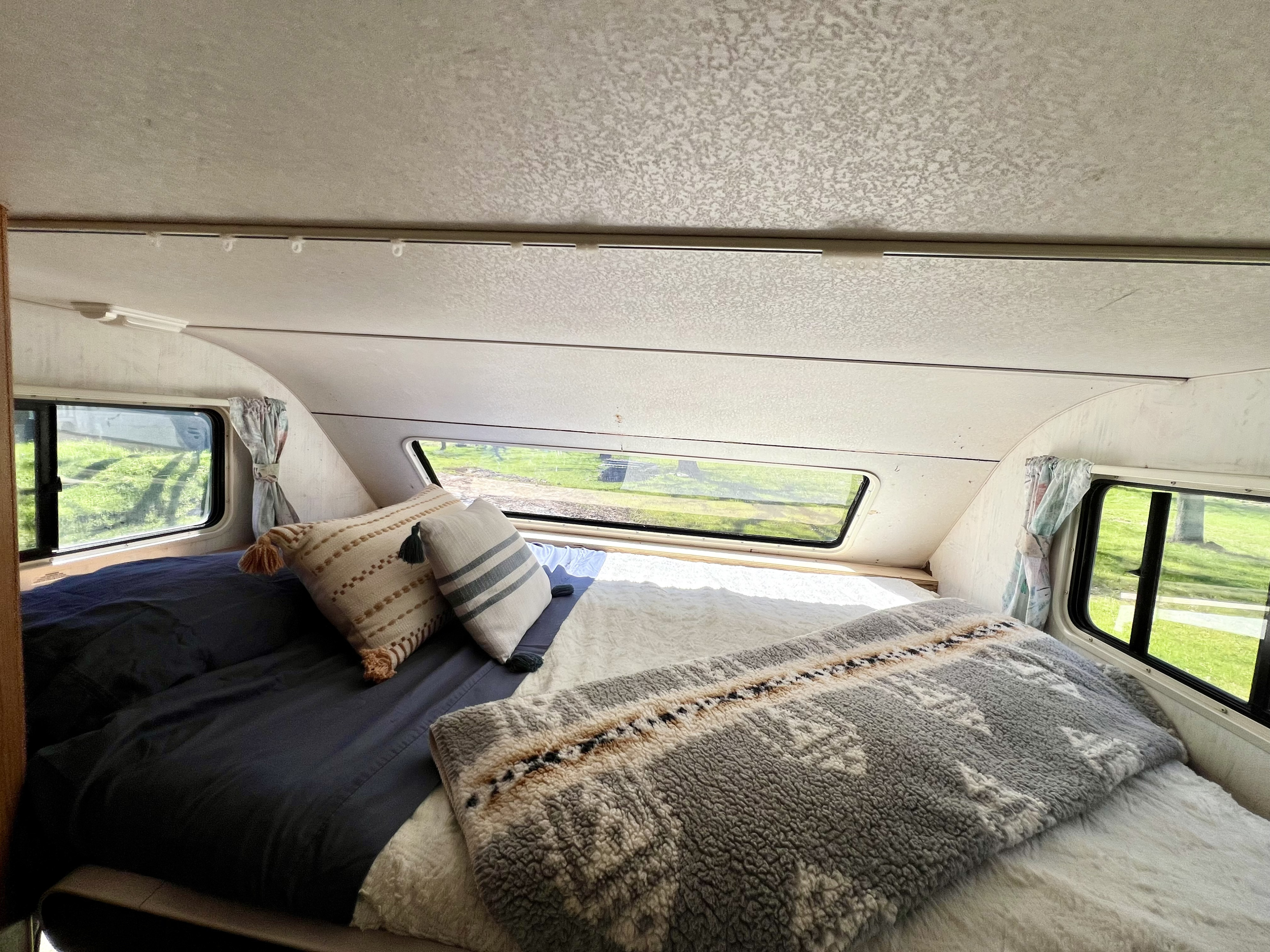 Cozy RV rental bedroom with a comfy bed, decorative pillows, and scenic window views.. Ford Econoline 1994