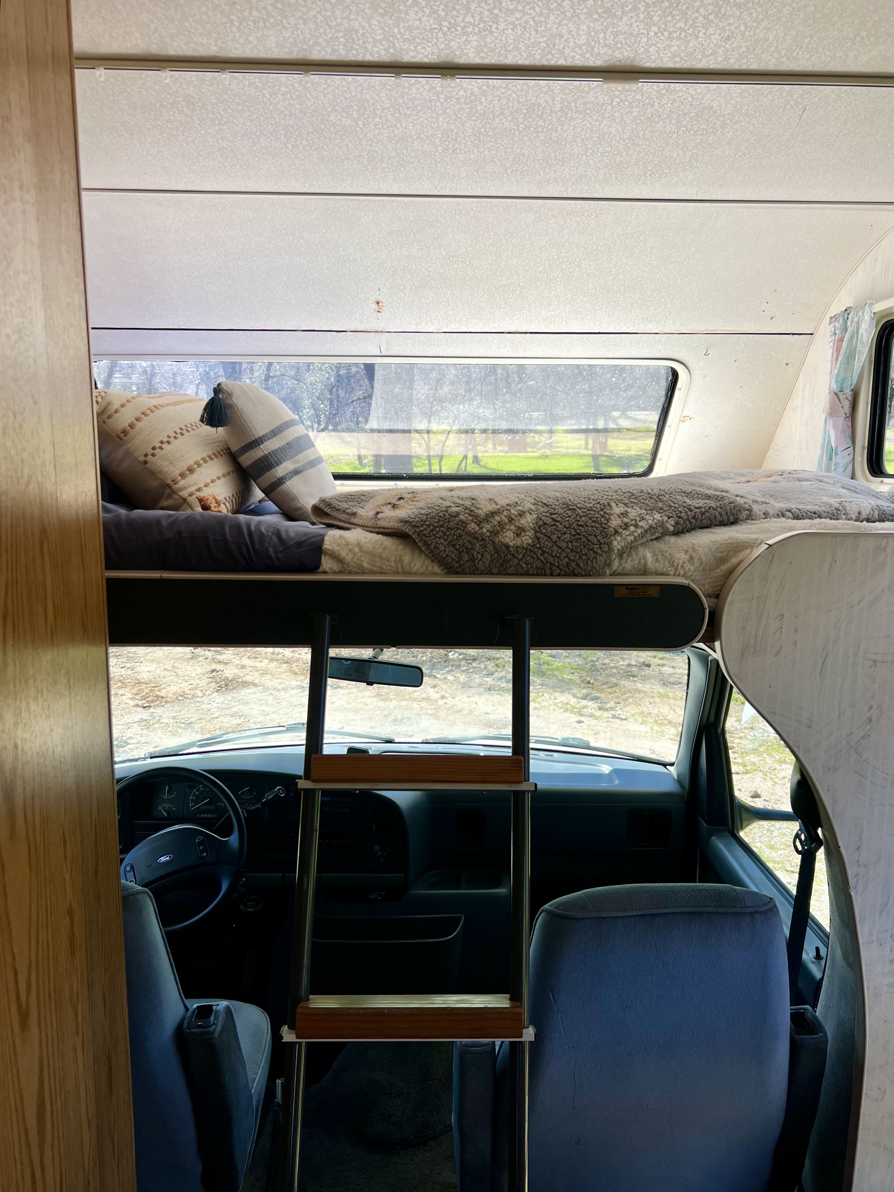 Spacious rv rental interior: look from inside a camper showing the top bunk bed, ladder, and driver's area.. Ford Econoline 1994