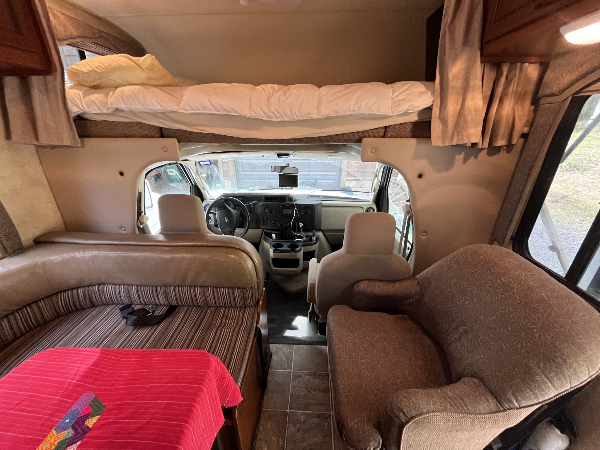 Inside a comfortable rv rental: front cockpit, overhead bunk bed, U-shaped dining, and armchair visible.. Thor Chateau 2013