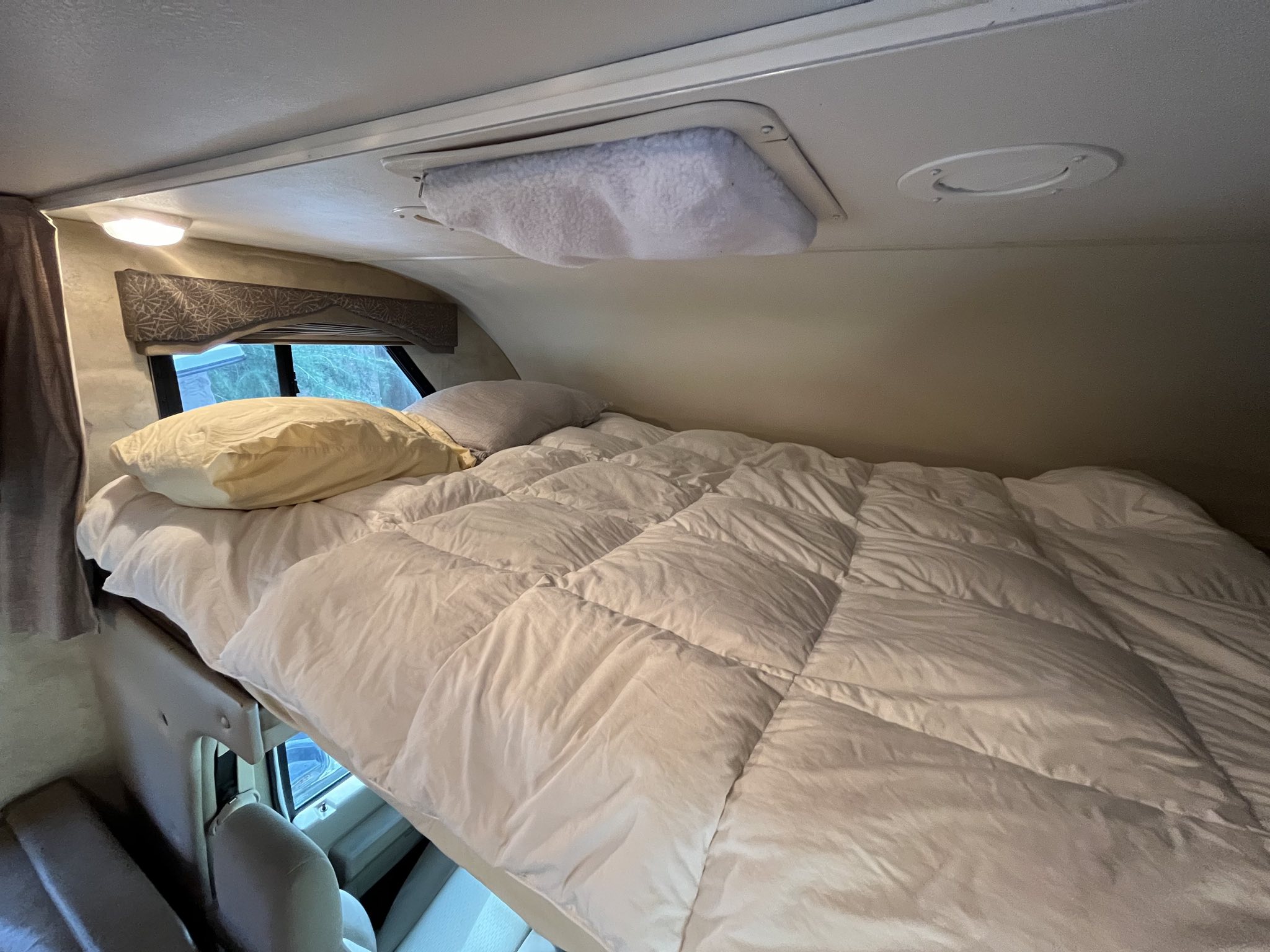 Comfortable cab-over bunk bed inside an RV rental, featuring a fluffy white comforter & pillows.. Thor Chateau 2013