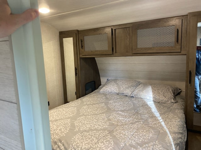 Step inside this cozy RV rental bedroom! Features a large bed with leaf patterned bedding, and ample overhead cabinets.. Forest River Wildwood 2021