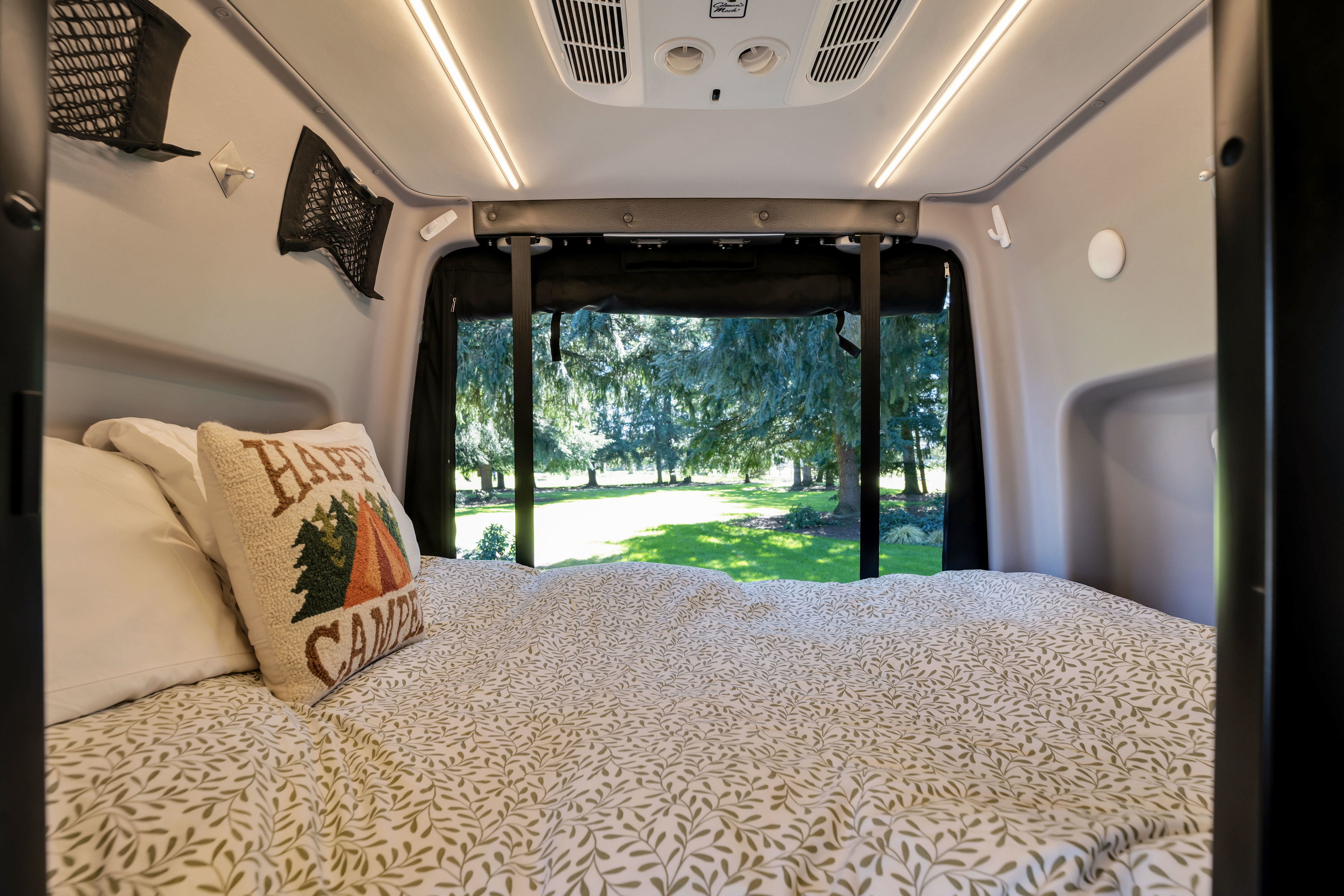 Comfortable RV rental bed with leafy bedding overlooking a serene outdoor view. Ideal for camping trips.. Winnebago Revel 2020