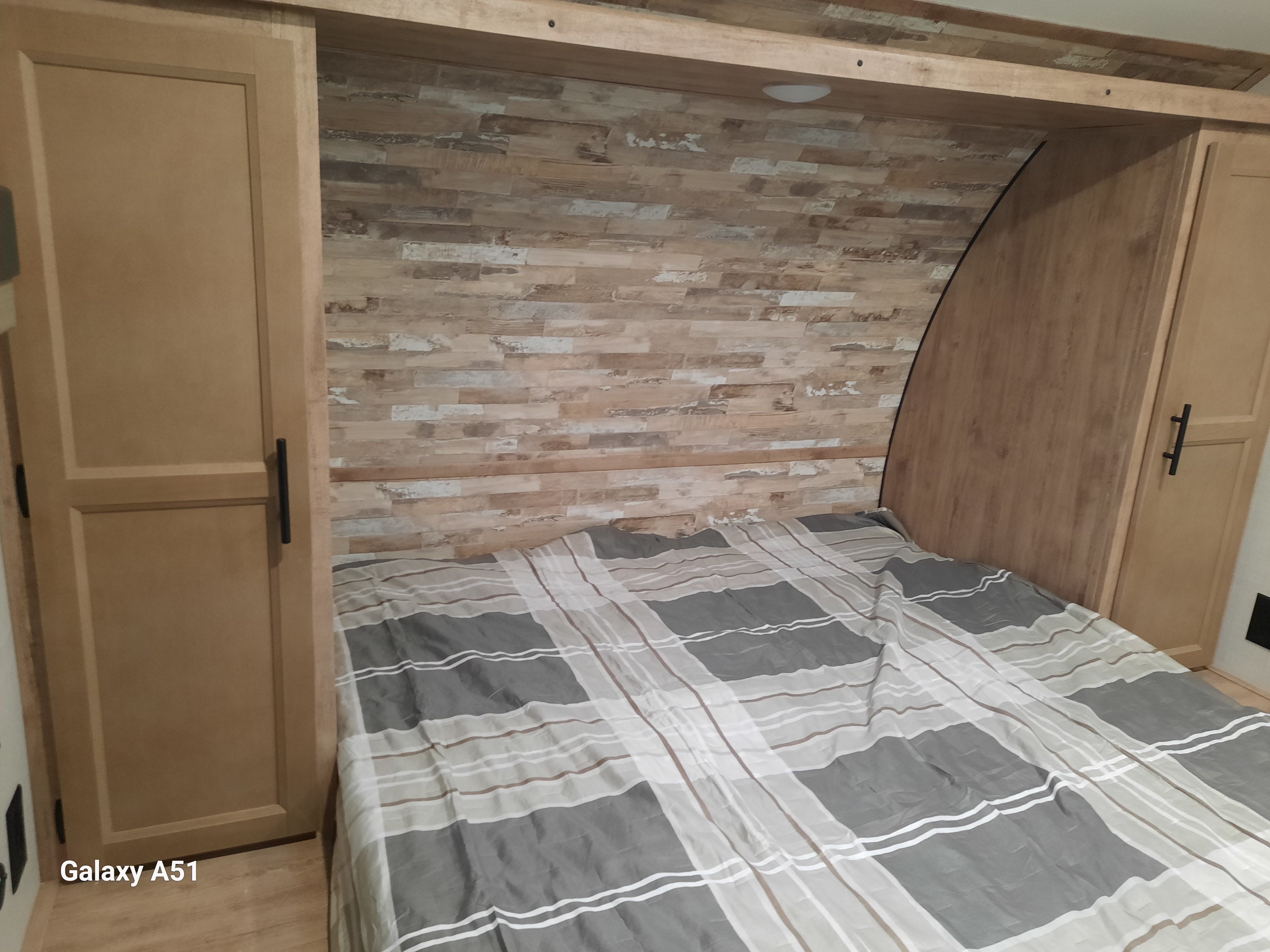 Inside an RV rental: a cozy bedroom features a striped bed, wood cabinets, and a textured headboard wall.. Gulf stream Kingsport 2024