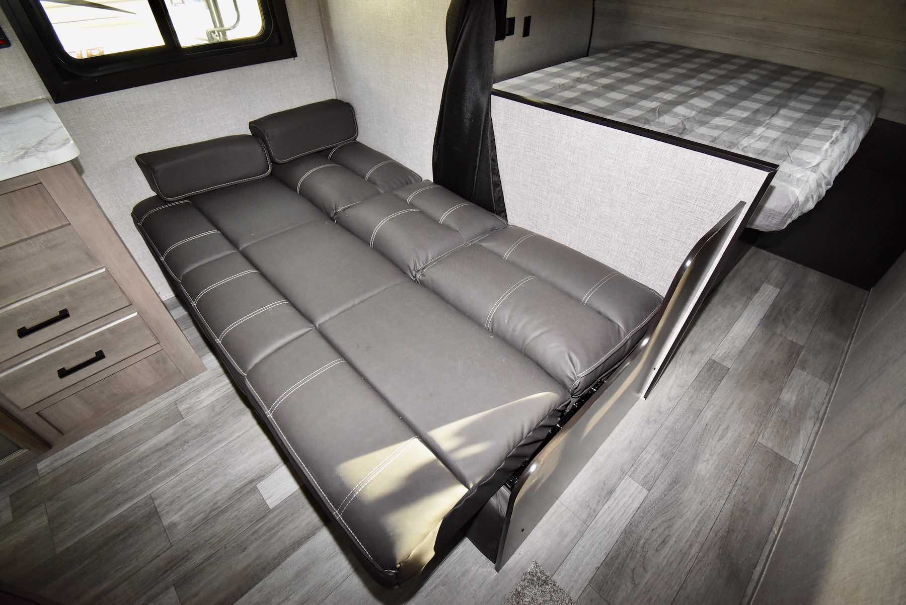 This RV rental offers a compact interior with a grey convertible sofa bed, a small cabinet, and a checkered bunk sleeping area.. Jayco Jay Flight 2022