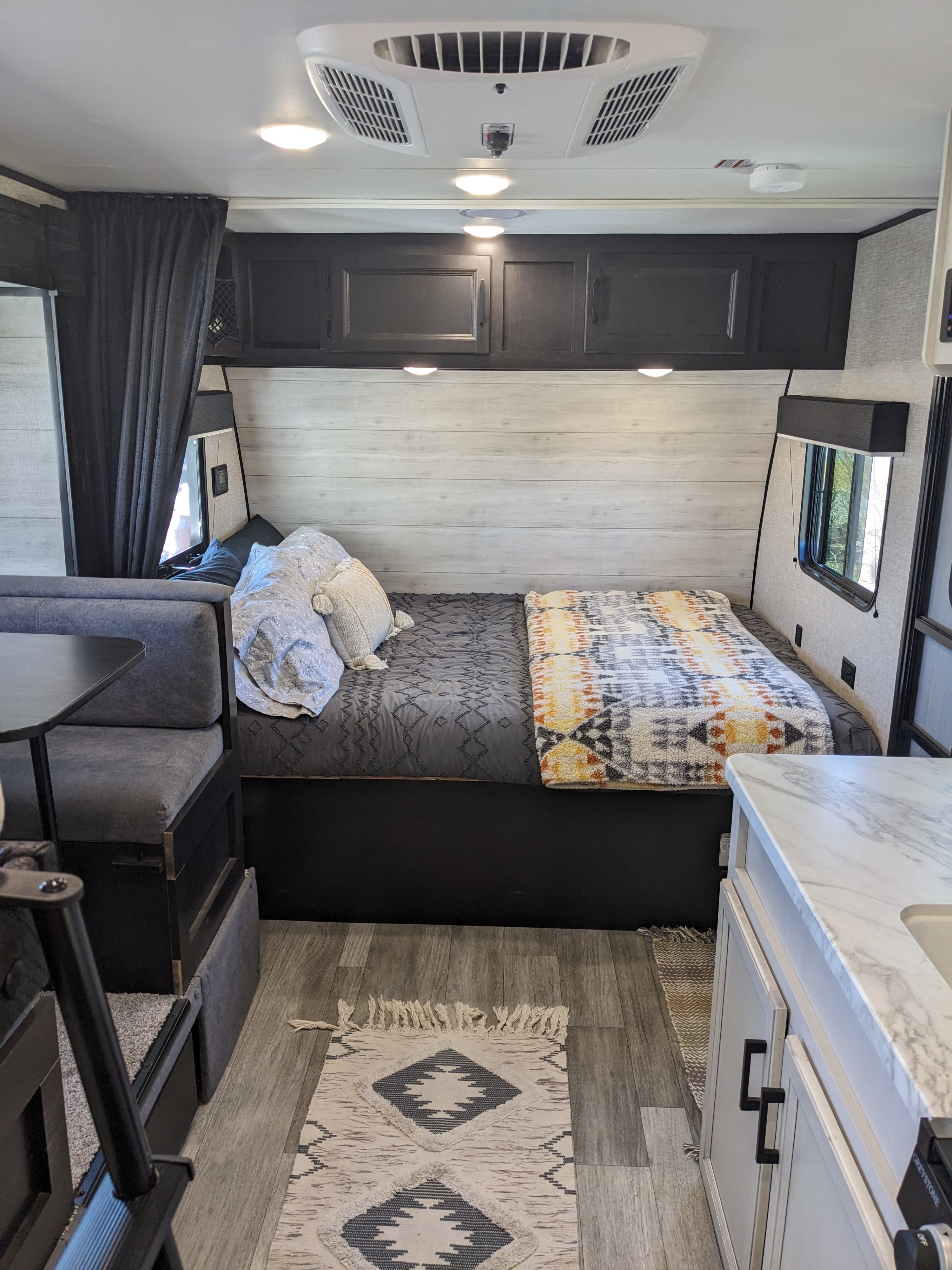 Experience a comfortable RV rental interior: bed, dinette, and kitchen with an AC unit and overhead cabinets. Cozy decor and lighting.. Jayco Jay Flight SLX Baja Edition 2023