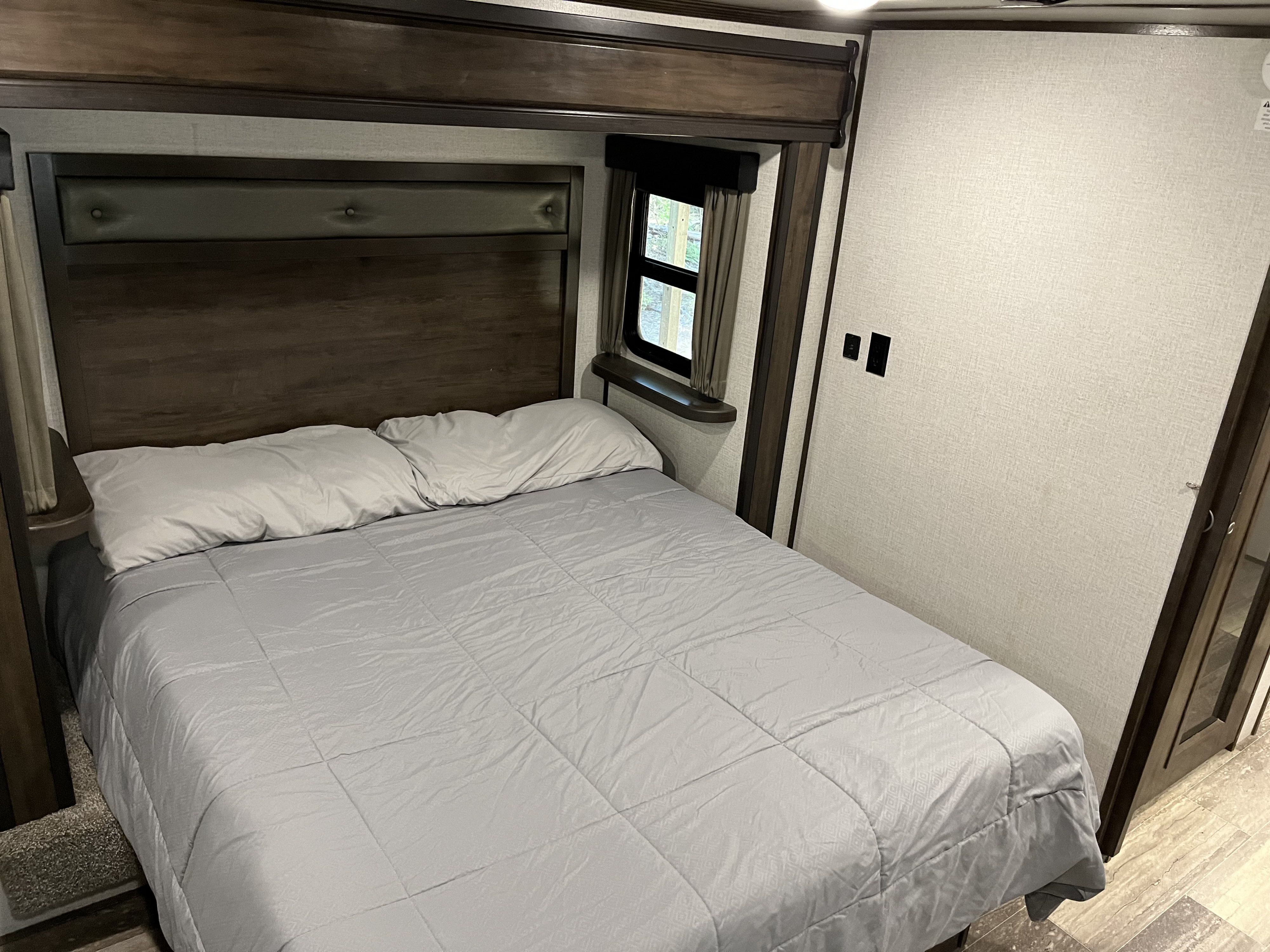 Comfortable RV rental bedroom featuring a cozy bed, wooden headboard, and window. Perfect for your travels.. Dutchmen Yukon 2021