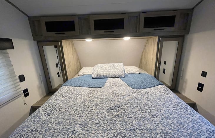 Cozy RV rental bedroom interior with a comfortable bed, overhead cabinets, and built-in mirrored wardrobes.. Forest River Cherokee Alpha Wolf 2022