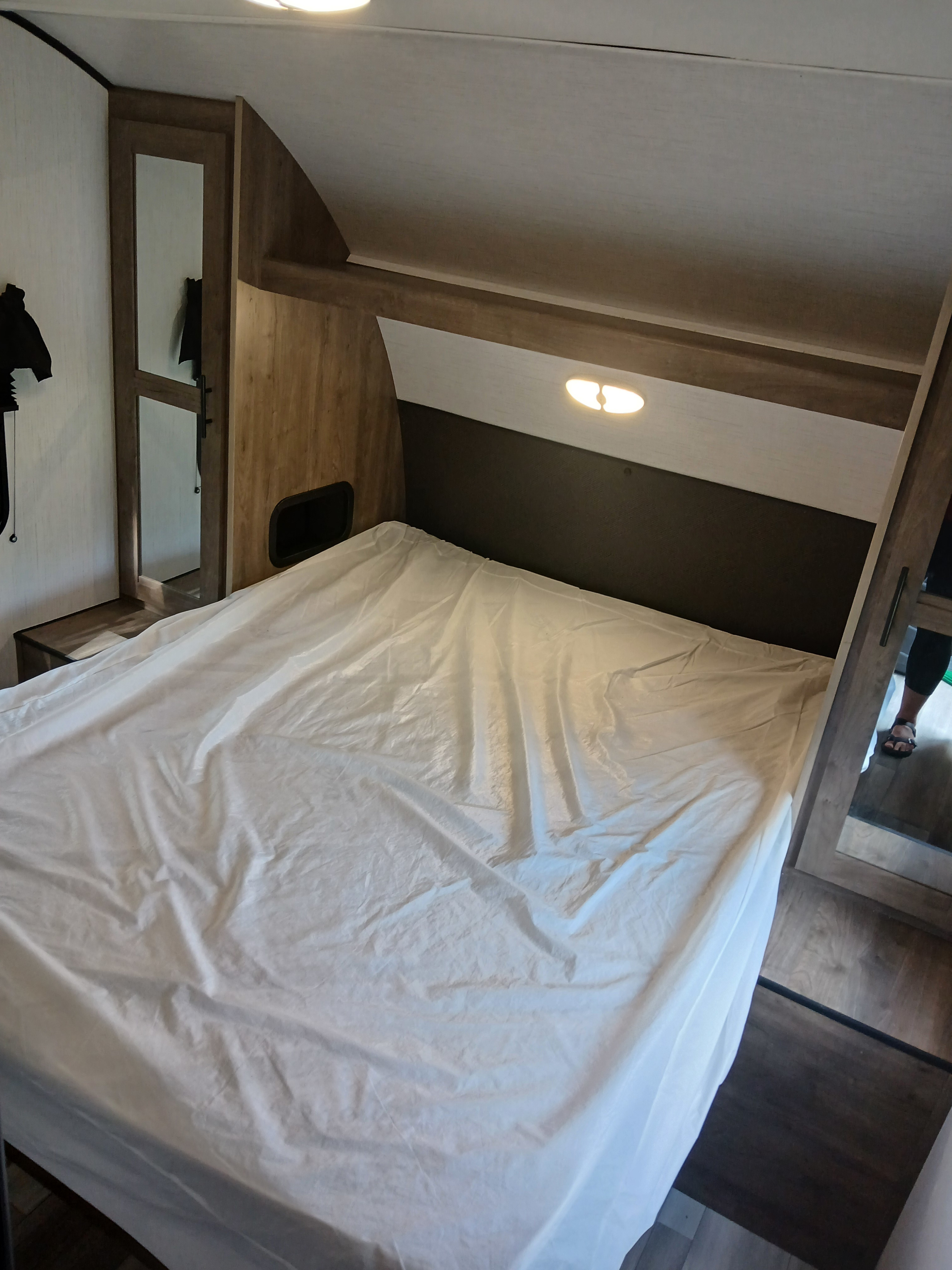 An RV rental bedroom showcasing a bed with white sheets, warm wood paneling, a reflective wardrobe, and overhead light.. Heartland RVs Pioneer 2022