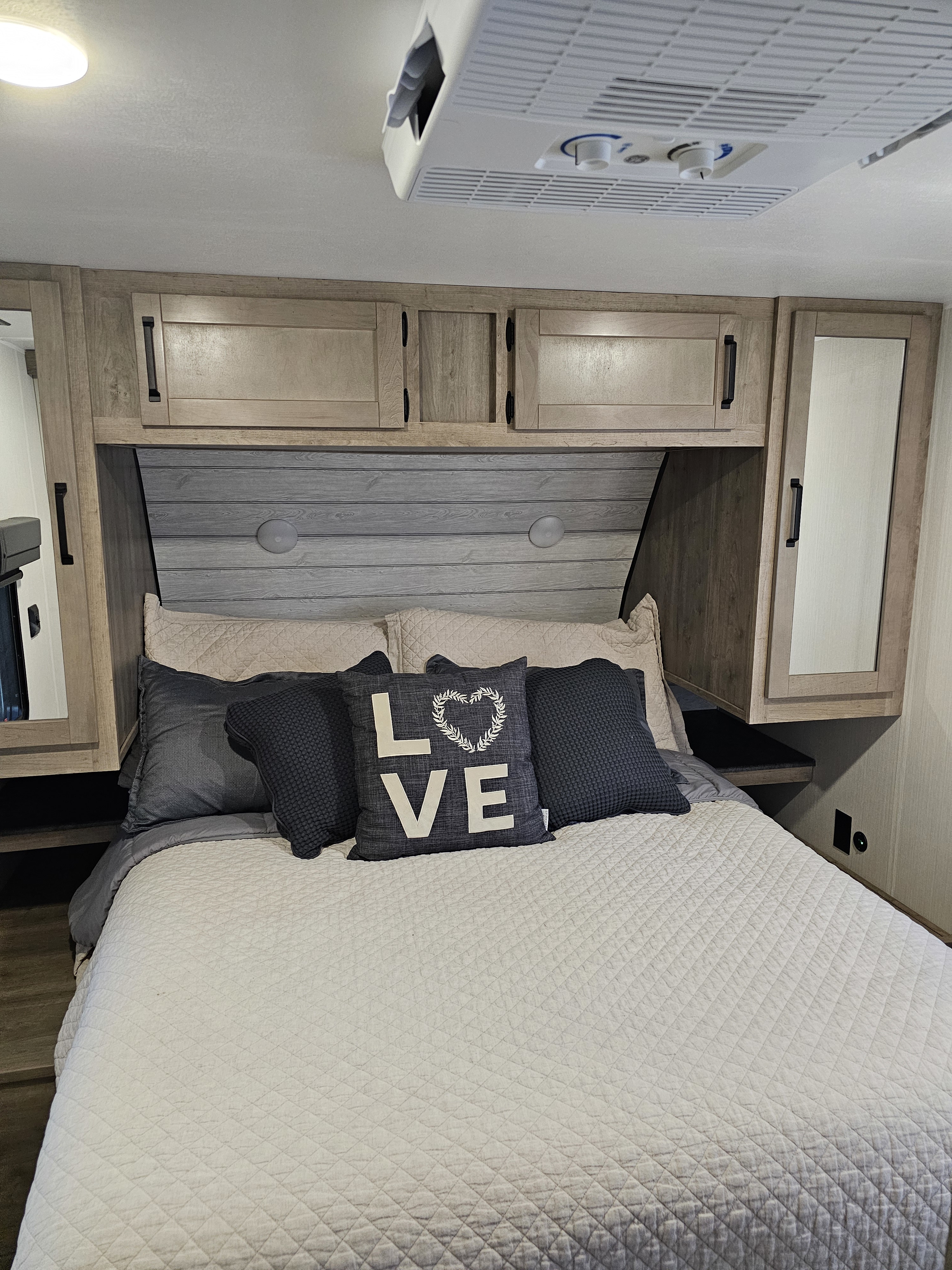 Cozy RV rental bedroom features a quilted bed, "LOVE" pillow, overhead cabinets, and AC unit for comfort.. Forest River Puma Palomino 2024