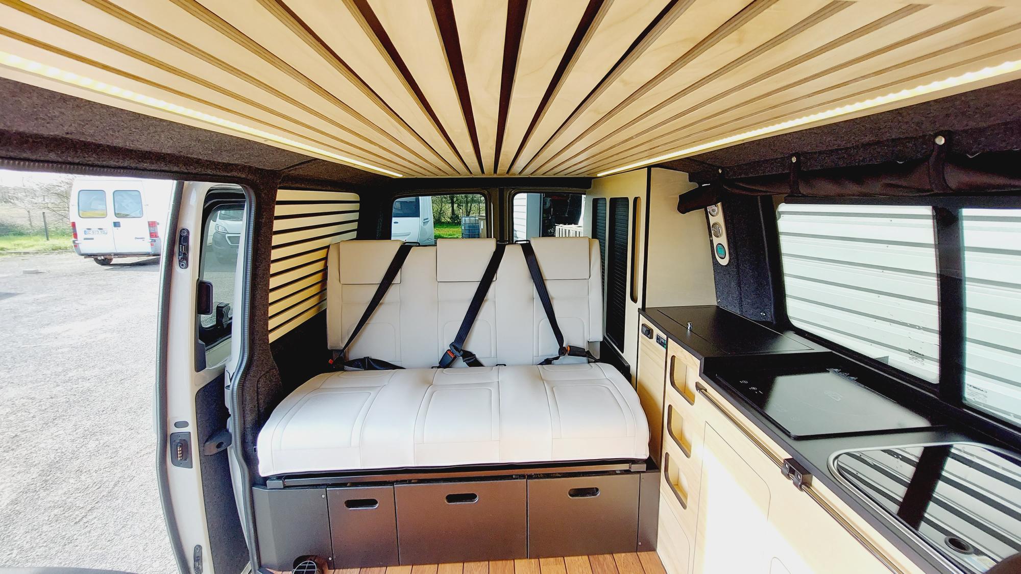 Step inside this stylish RV rental, featuring a comfortable bed, passenger seating, and a compact kitchen.. Volkswagen T6.1 2023