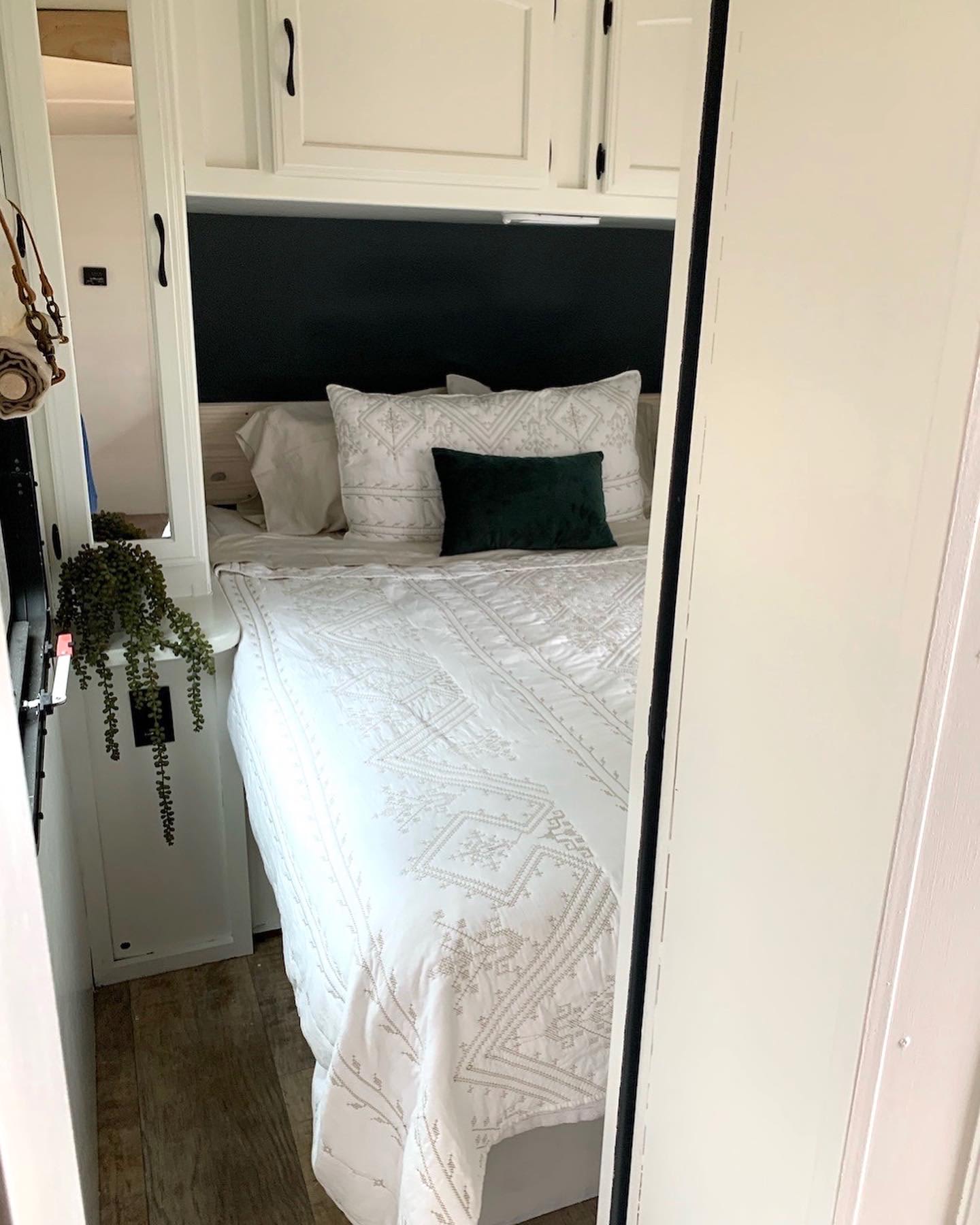 Step into this cozy RV rental bedroom: white patterned bedding, dark headboard, and wood-look floors. Features overhead cabinets.. Jayco White Hawk 2016
