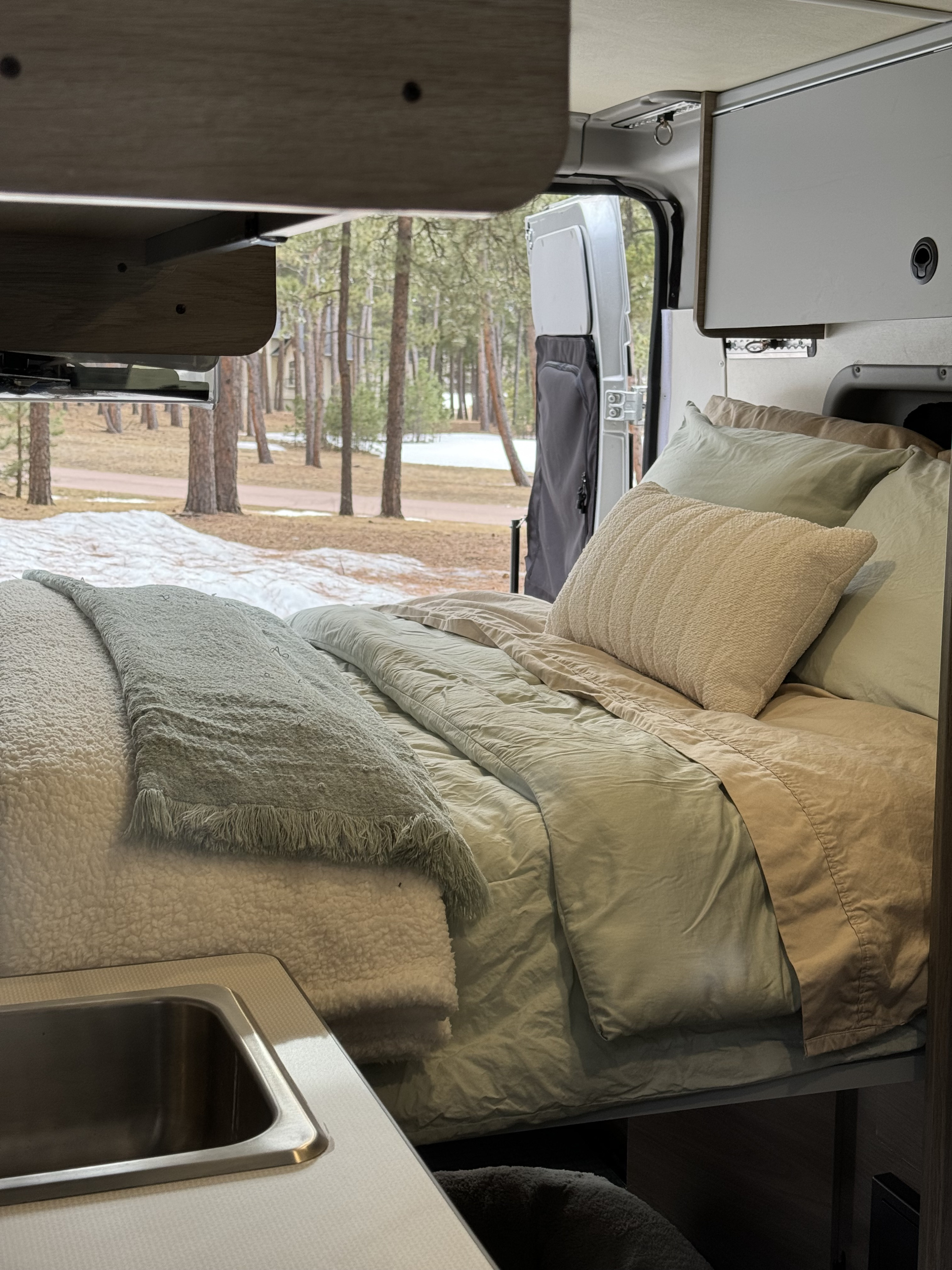 An inviting RV rental interior with a cozy bed and small sink, overlooking a quiet, snow-dusted forest.. Winnebago Solis 2022