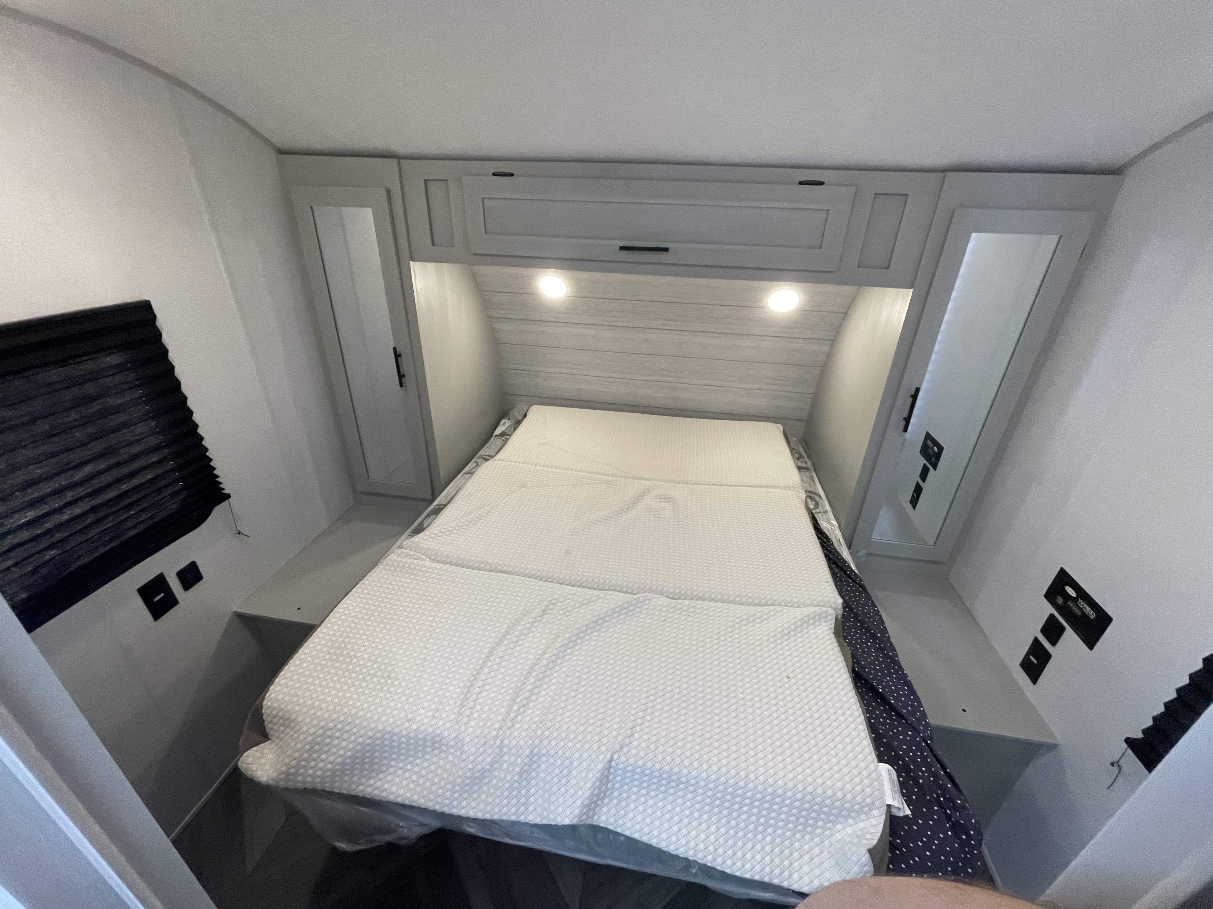 A compact, modern RV rental bedroom featuring a fresh, unmade bed, overhead cabinets with lights, and side storage.. Forest River Salem Cruise Lite 2022