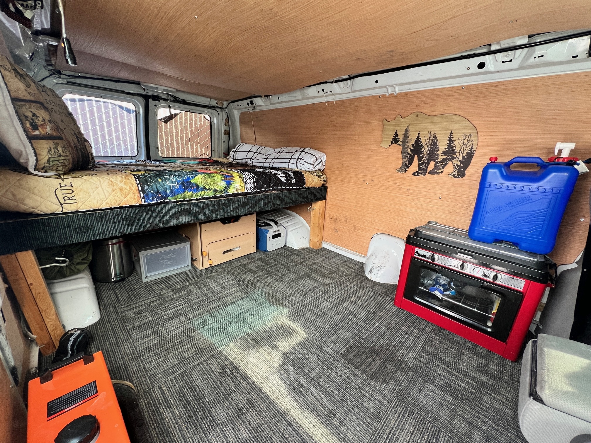 RV rental: Cozy van interior with bed, red portable oven/stove, and organized storage for travel.. Ford Econoline 150 1997