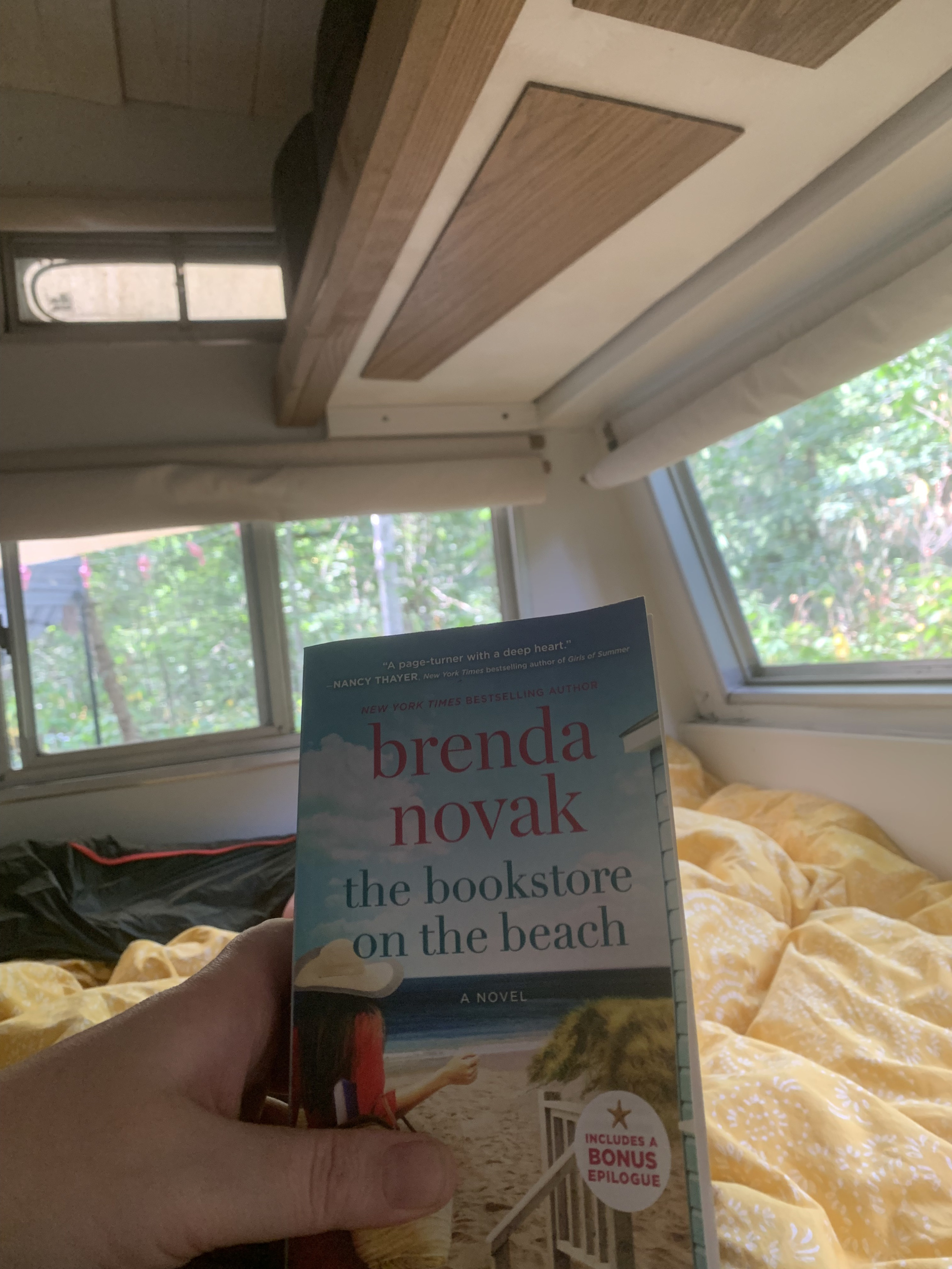 Cozy RV rental reading: "The Bookstore on the Beach" by Brenda Novak, enjoying quiet time inside an RV with green views.. Vanguard Industries other 1972