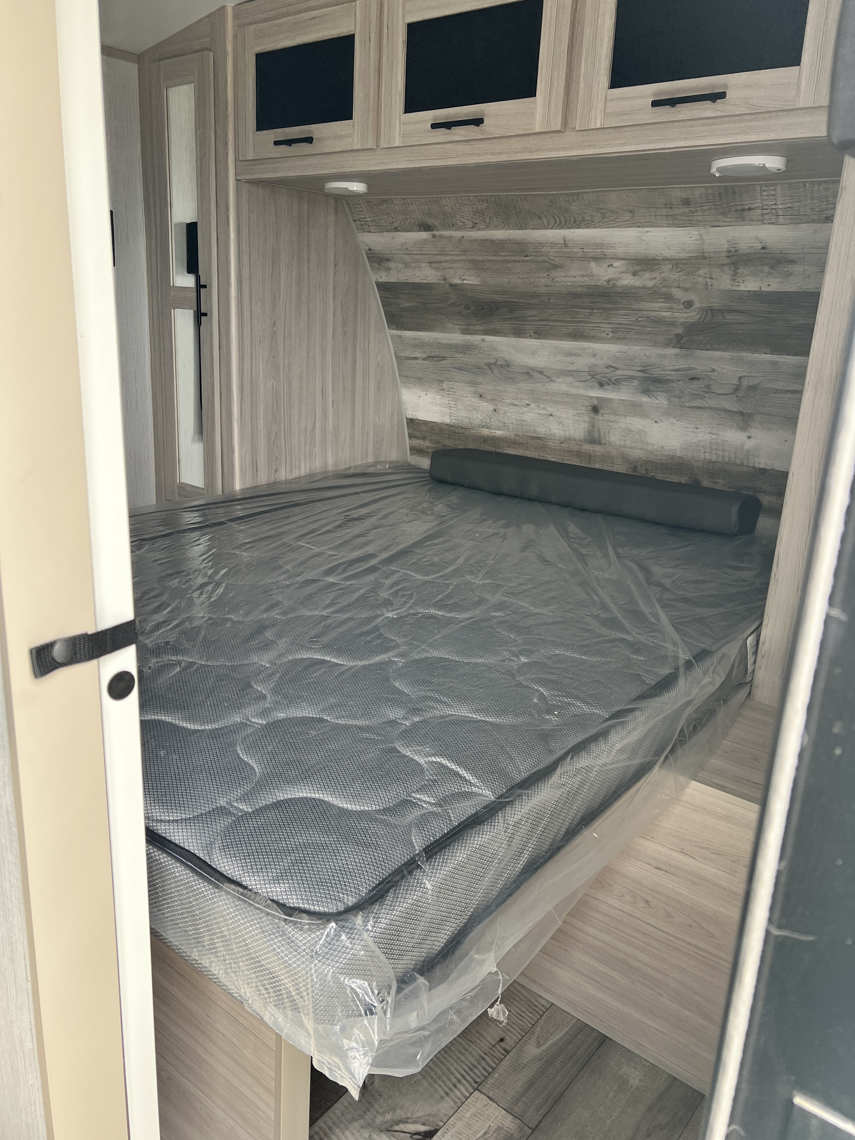 Spacious RV rental bedroom with a new grey mattress, sleek wood-grain walls, and convenient overhead storage cabinets.. Heartland RVs Sundance Ultra Lite 2022