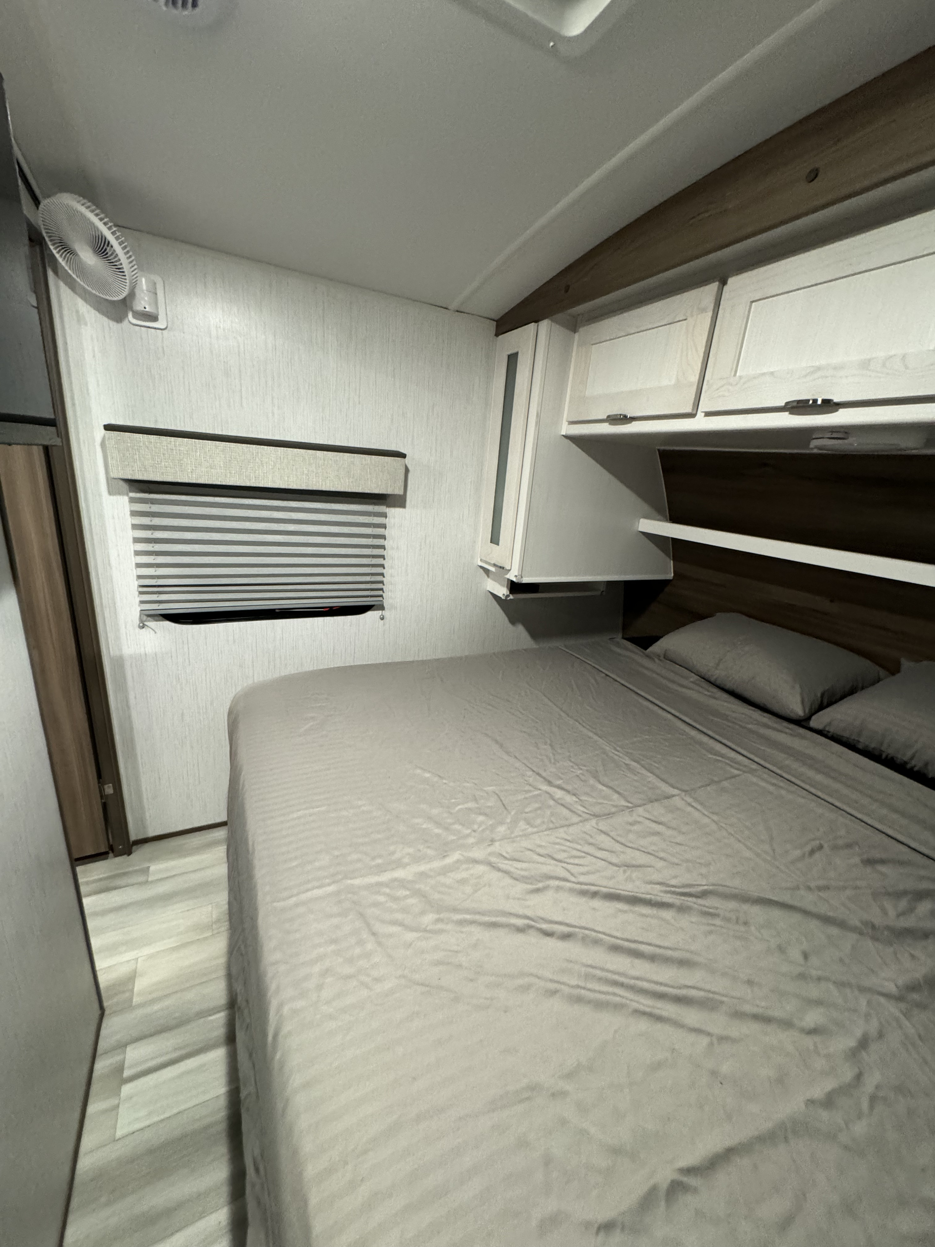 RV rental bedroom with light walls, wood-look floor, comfortable bed, overhead storage, and window blinds.. Cruiser RV MPG 2023