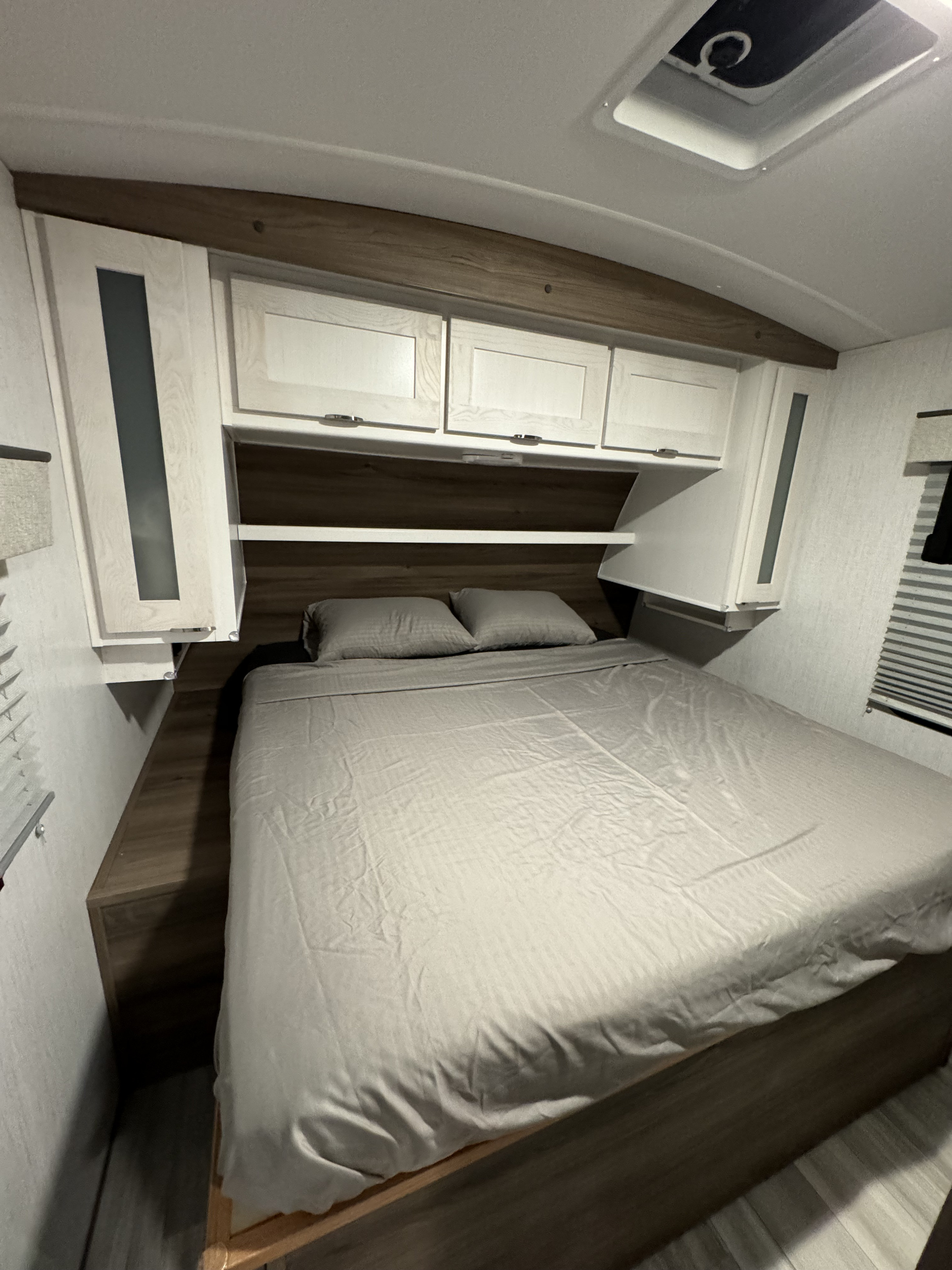 Spacious RV rental bedroom featuring a large bed, overhead storage cabinets, and modern wood-look finishes. Ready for your adventure.. Cruiser RV MPG 2023