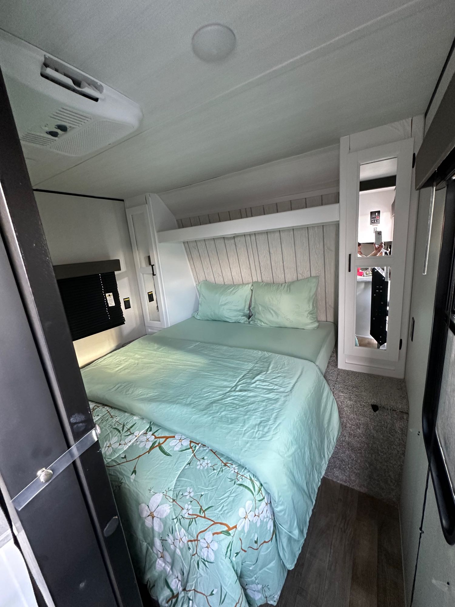 RV rental bedroom with mint green bedding on a queen bed, mirrored cabinet, and ceiling AC. Cozy interior for travel.. Keystone RV Hideout 2022