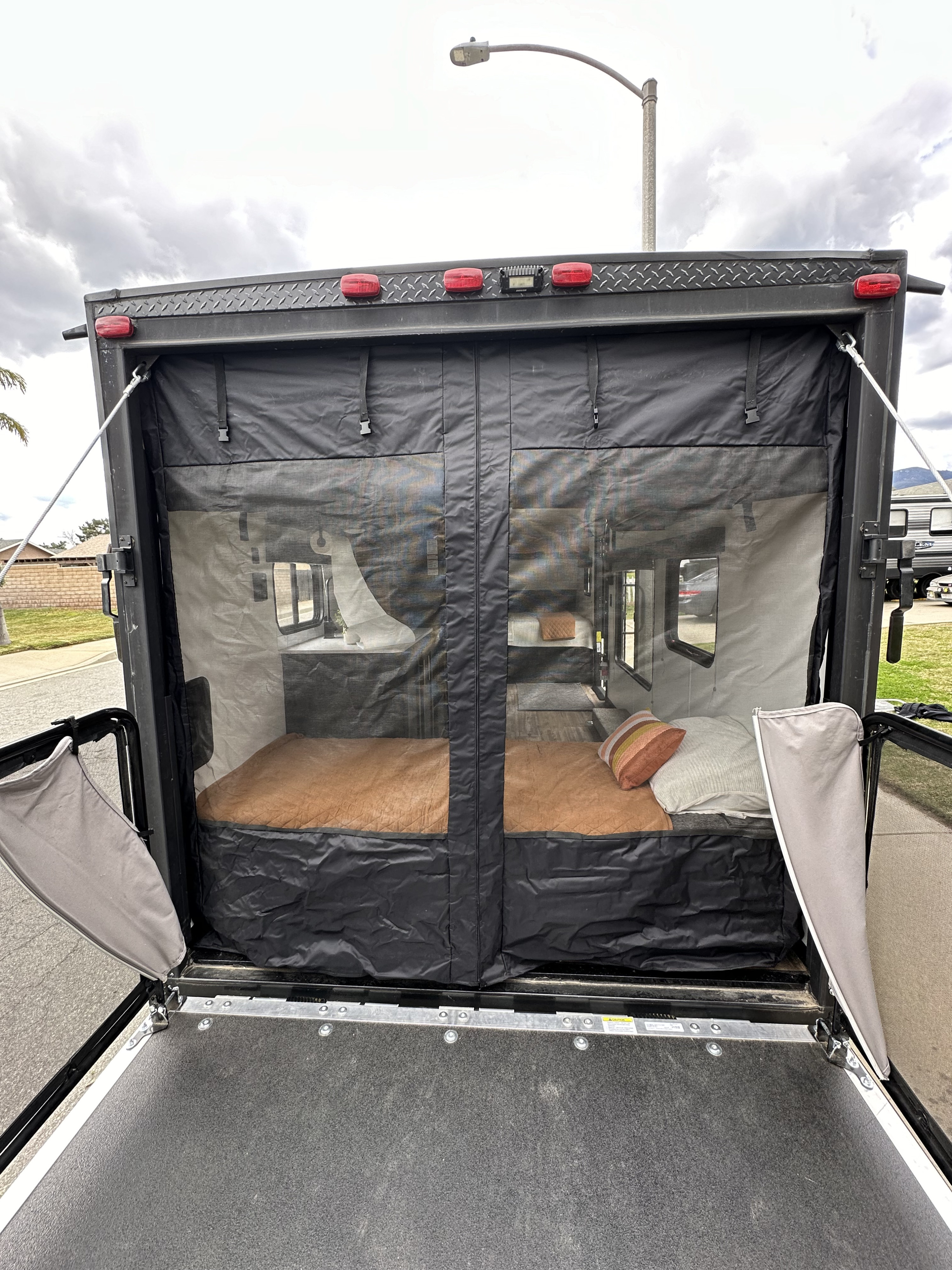 RV rental toy hauler with ramp door open, revealing a screen enclosed patio and twin beds inside. Perfect for outdoor living!. Forest River Cherokee Wolf Pup 2021