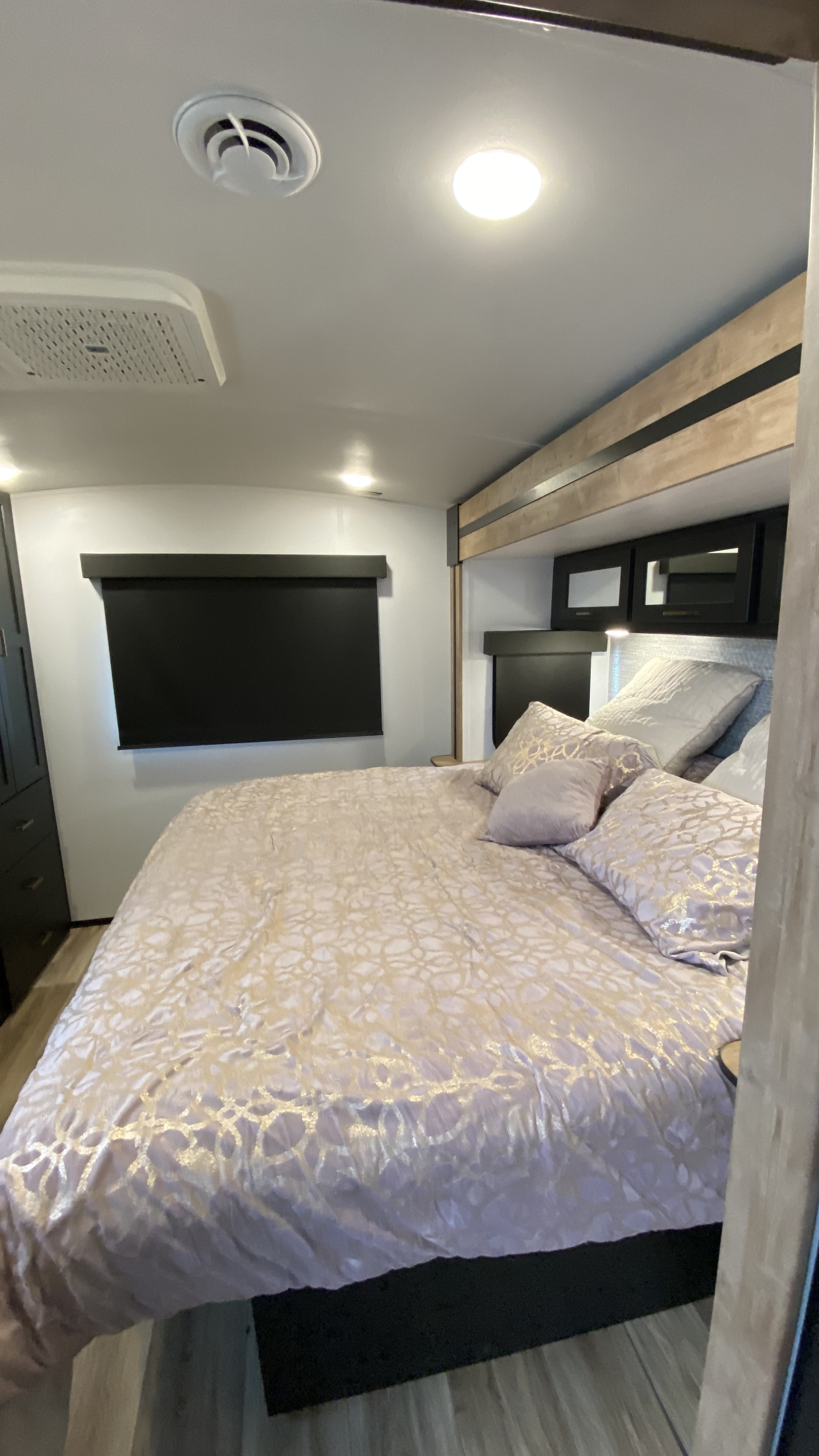 RV rental bedroom showcasing a spacious bed with elegant bedding, overhead cabinets, and modern lighting.. Keystone RV Outback 2023