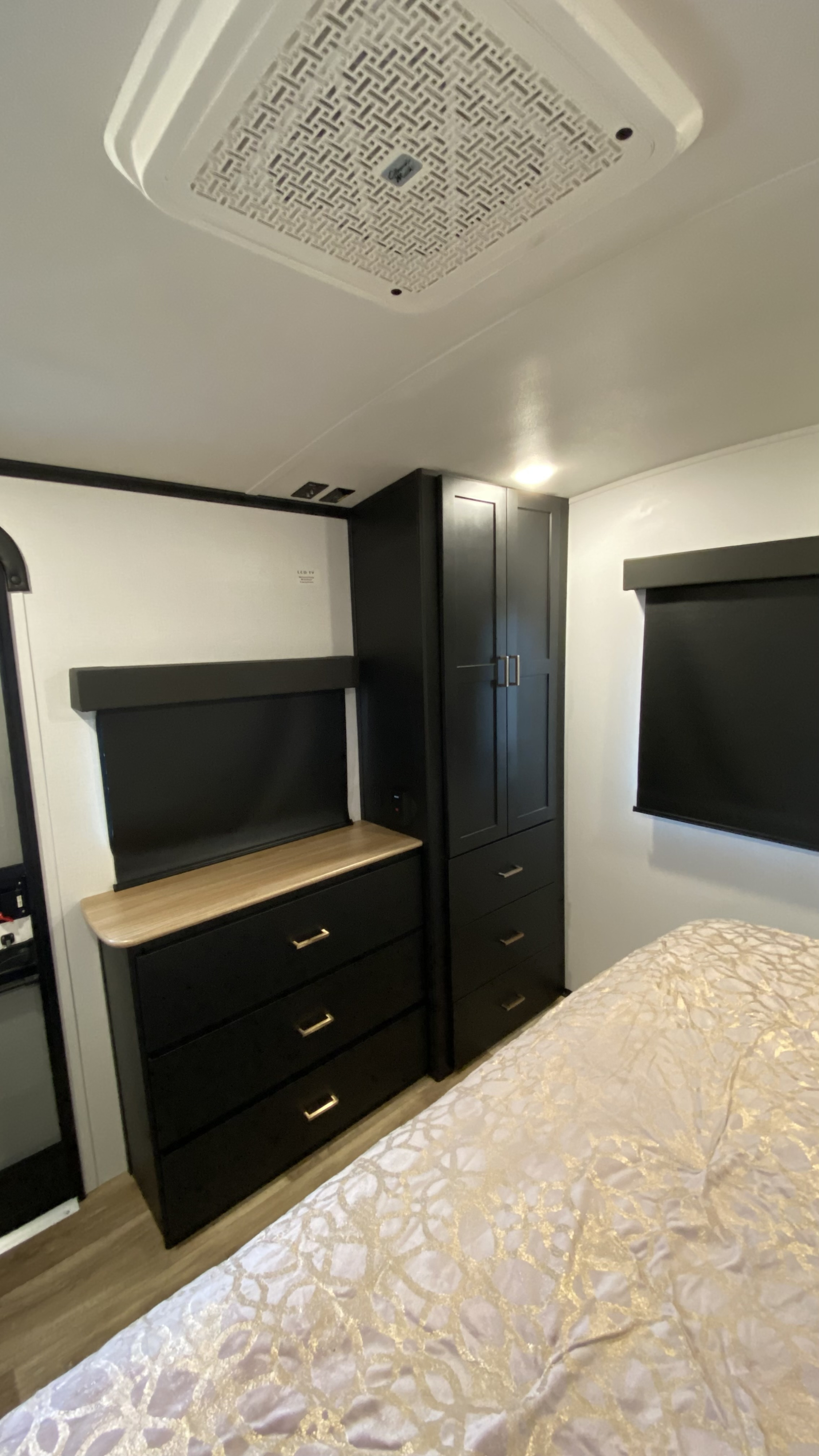 Cozy RV rental bedroom featuring modern black cabinetry, a light wood counter, patterned bed, and overhead AC.. Keystone RV Outback 2023