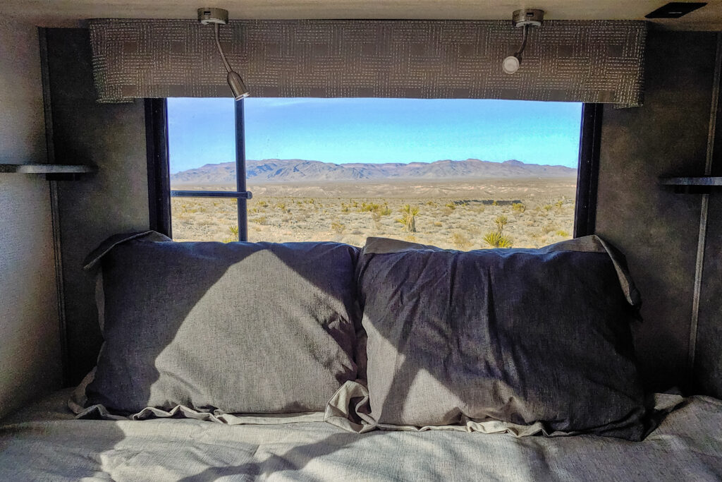 RV rental interior: A cozy bed sits before a window overlooking a vast desert, distant mountains & Joshua trees.. Forest River Sunseeker 2022