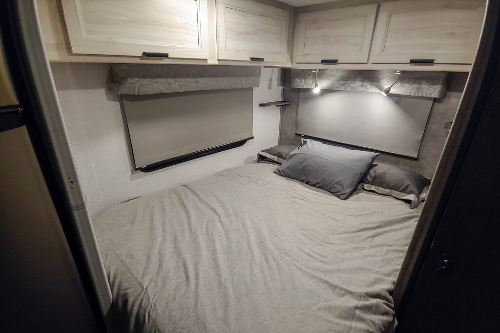 Cozy RV rental bedroom featuring light wood cabinets, a neatly made bed, and modern reading lights for a comfortable journey.. Forest River Sunseeker 2022