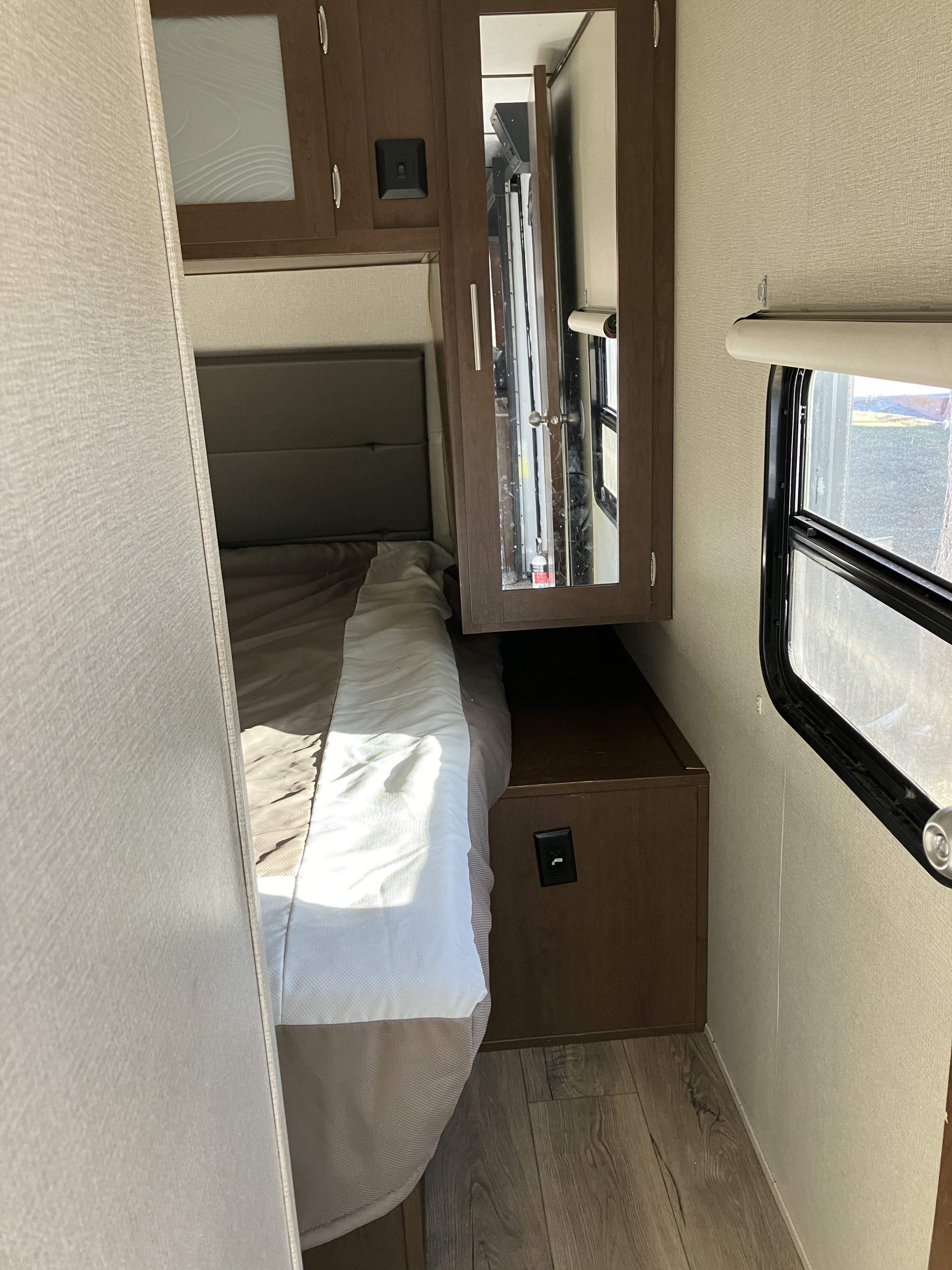 Cozy RV rental bedroom with a bed, overhead cabinets, and a side window, showcasing a compact and comfortable living space.. Forest River Wildcat 2019