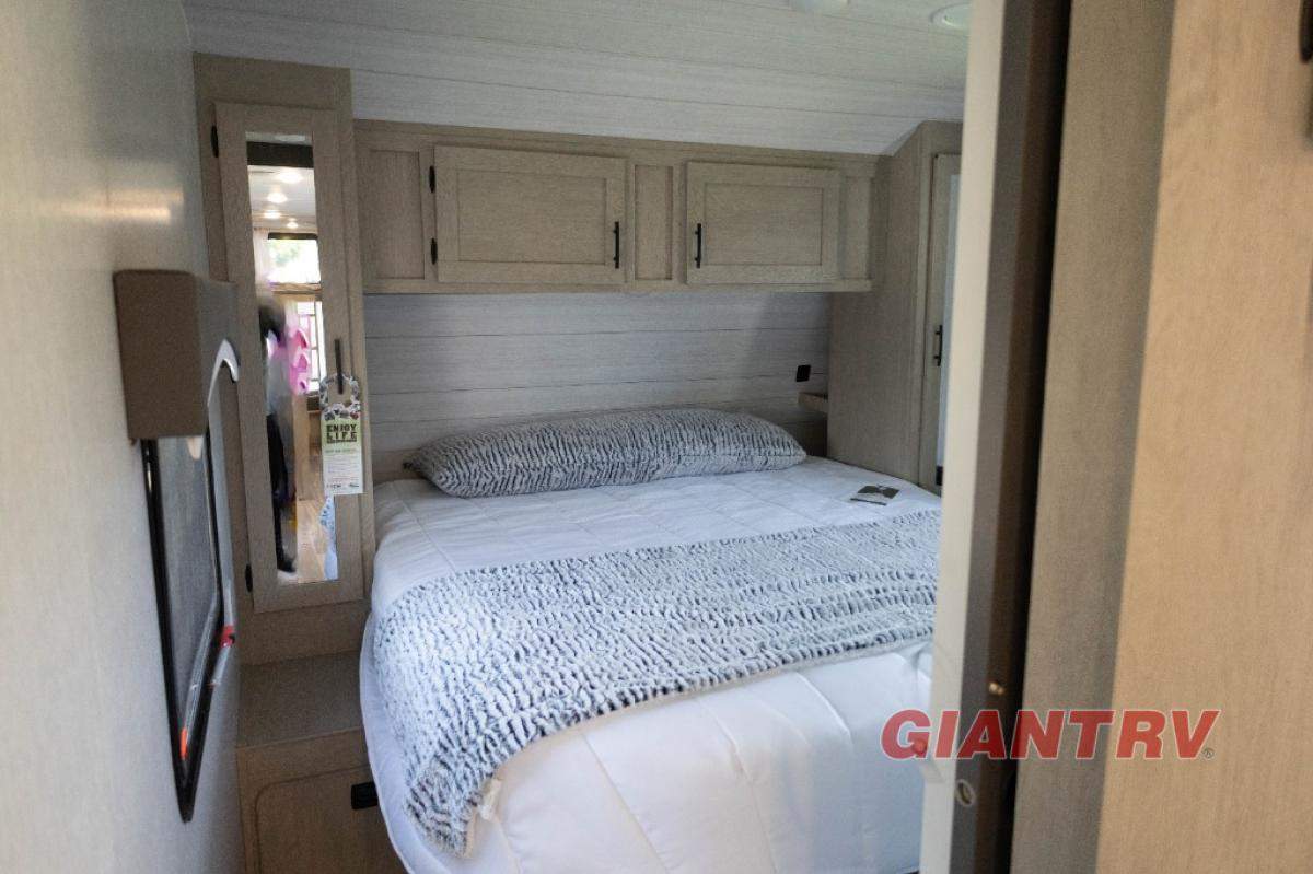 This inviting RV rental features a compact bedroom with a cozy bed, soft gray blanket, overhead cabinets, and a mirrored wall.. Forest River Evo CSJT2650G 2023