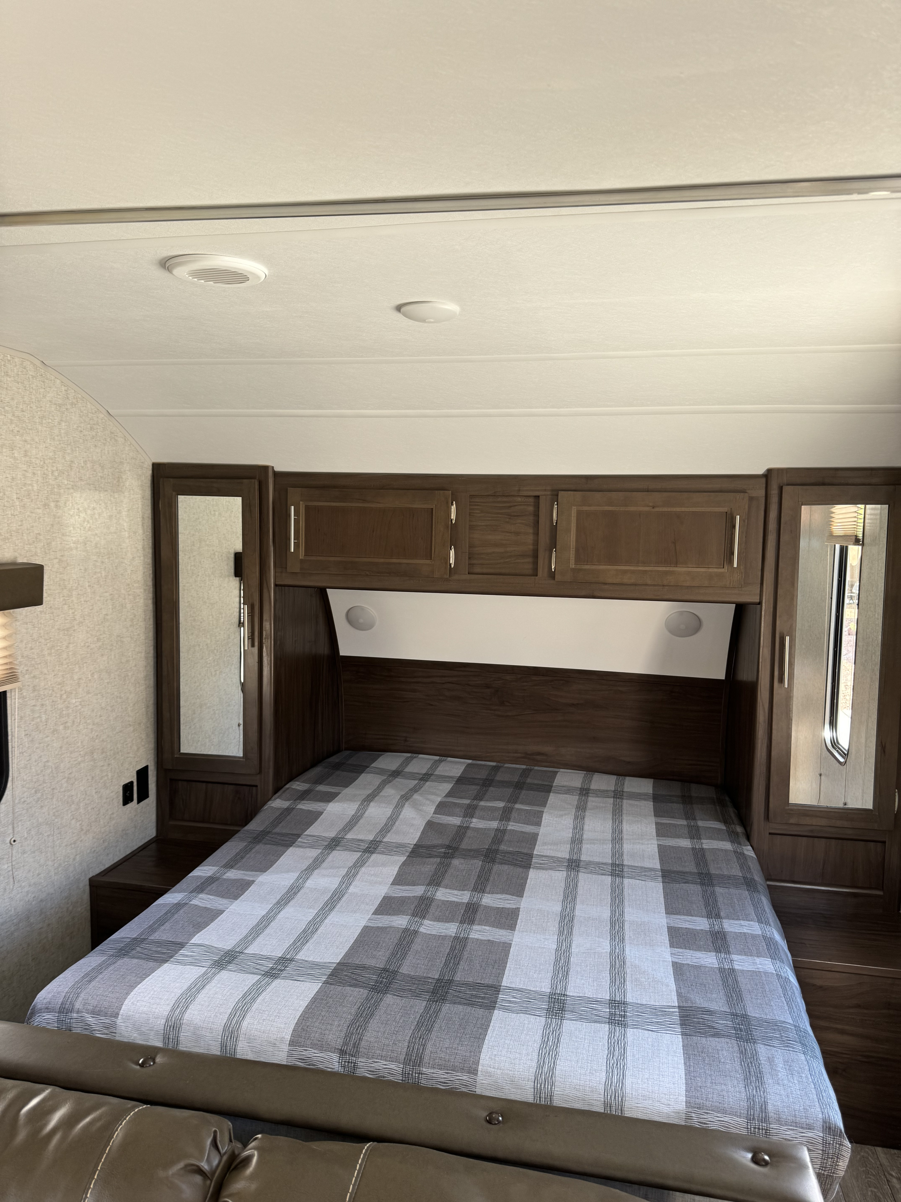 Cozy RV rental bedroom with a plaid bed, dark wood overhead cabinets, and mirrored wardrobes.. Forest River Cherokee 2018