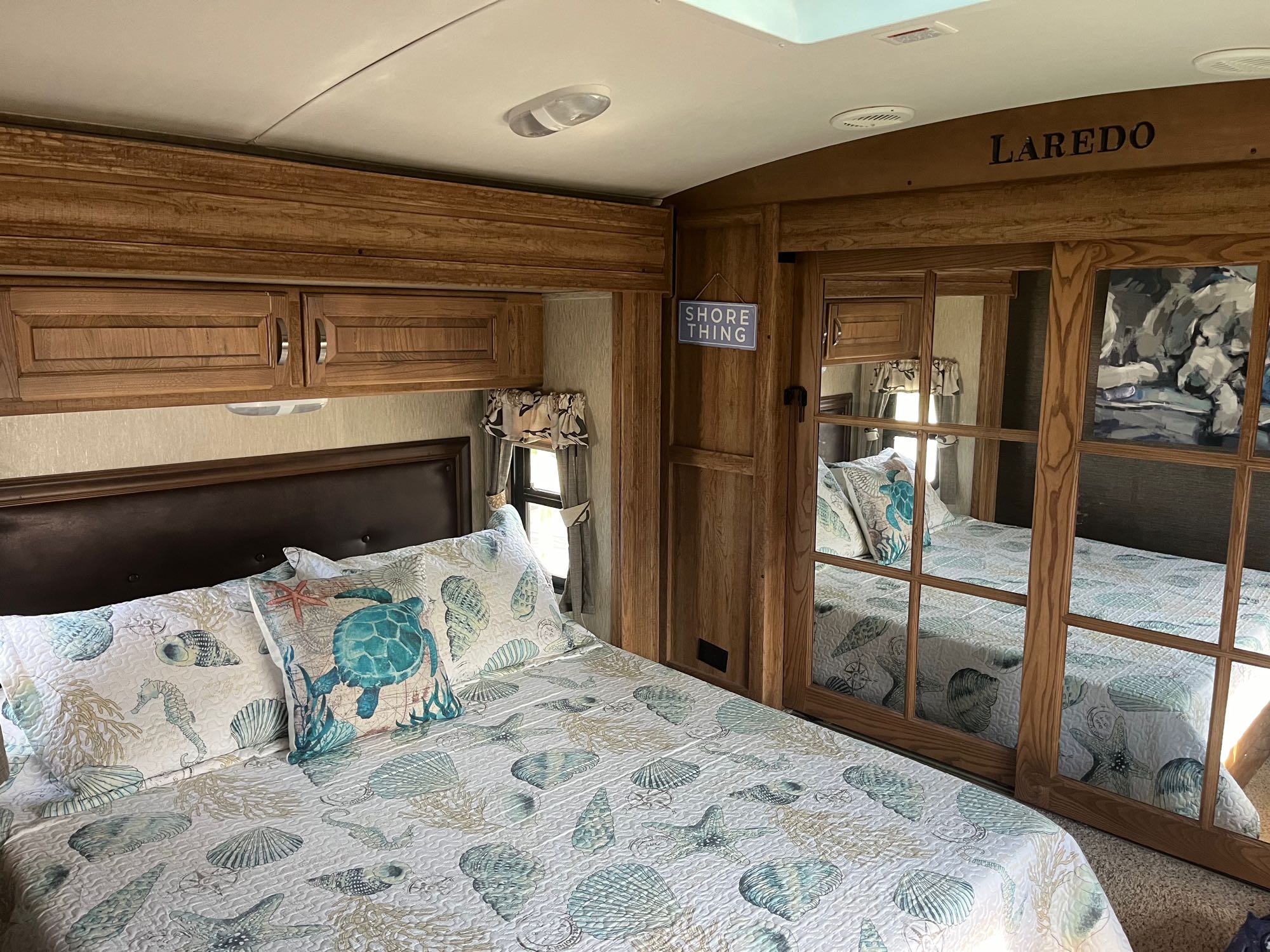 Cozy RV rental bedroom with coastal decor. Features a bed, wooden cabinets, and mirrored closet doors.. Keystone Laredo 2015