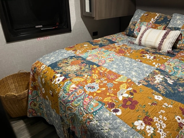 Inside a cozy RV rental bedroom: a vibrant patchwork quilt covers the bed, next to an emergency exit window.. Highland Ridge RV Open Range 2023
