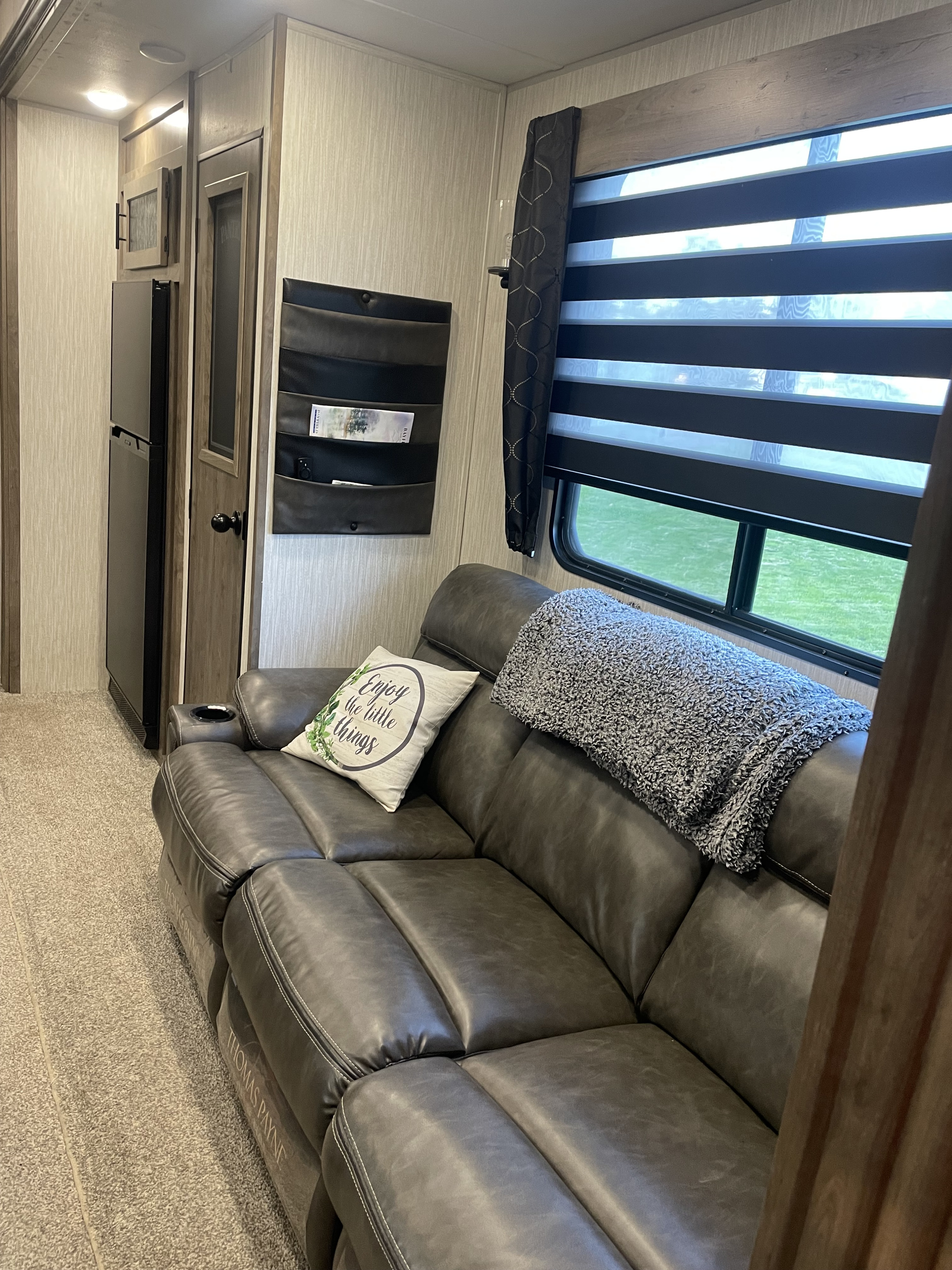 Cozy RV rental living area featuring a gray leather sofa, a window with shades, and convenient wall storage.. Forest River Cherokee Wolf Pack Toy Hauler 2021