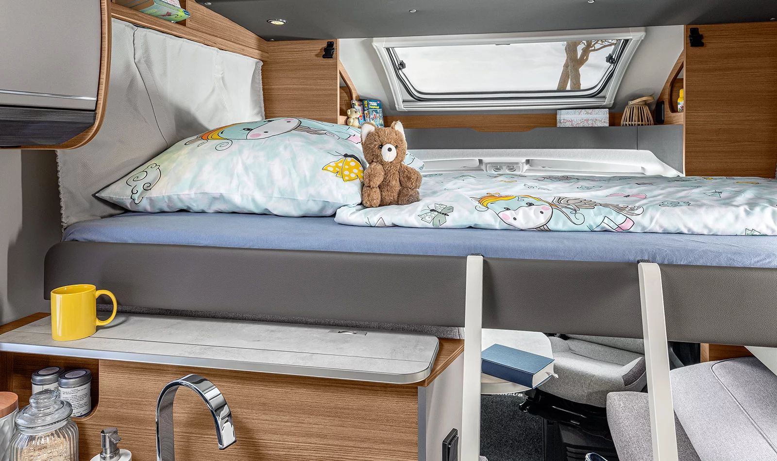 Cozy RV rental bunk bed for kids, featuring a cute unicorn bedding, teddy bear, and integrated sink area below.. Knaus live wave 2024