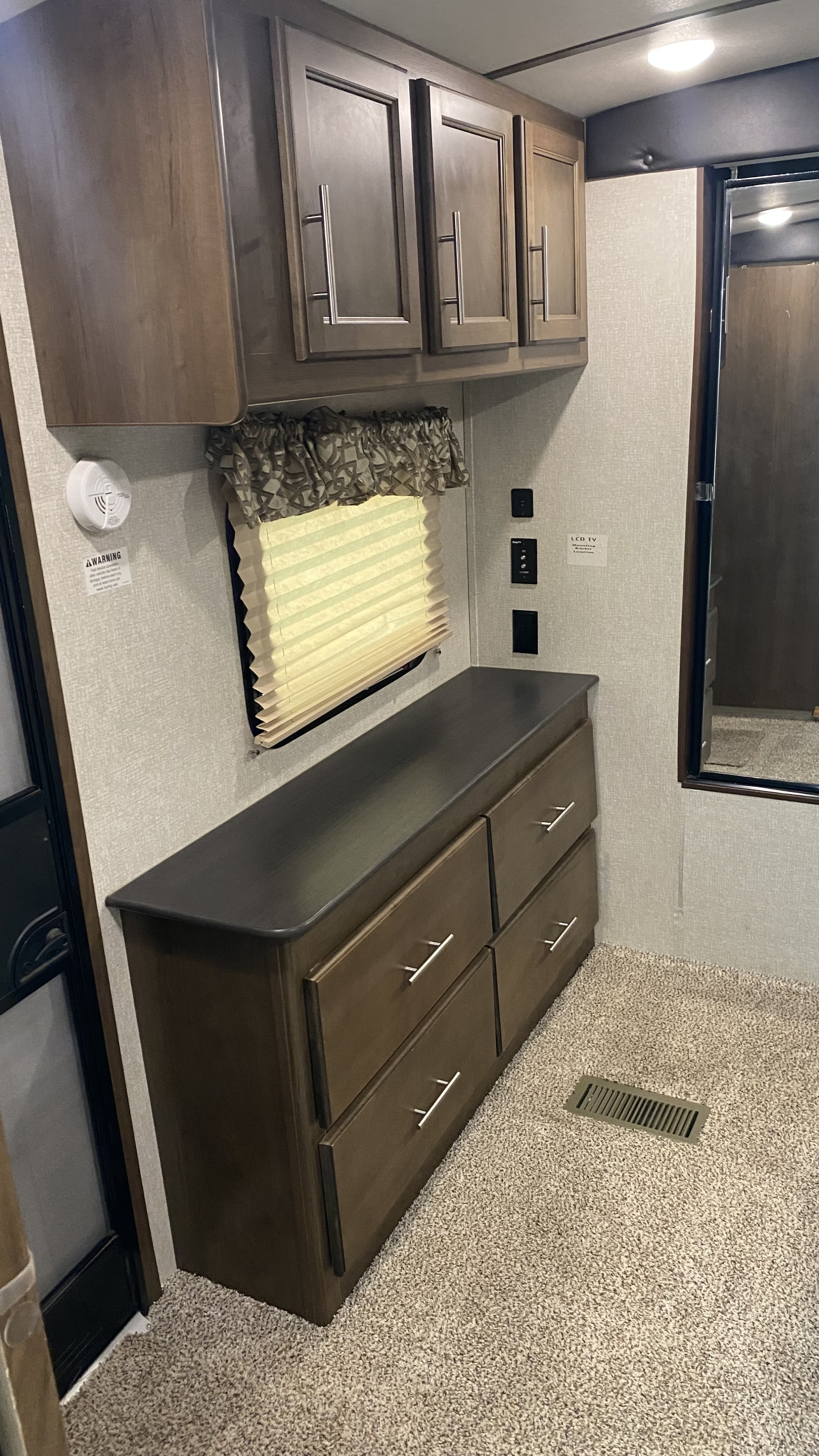 RV rental interior details: wood cabinets, dresser with silver pulls, carpeted floor, and wall-mounted utilities.. Keystone RV Cougar 2019