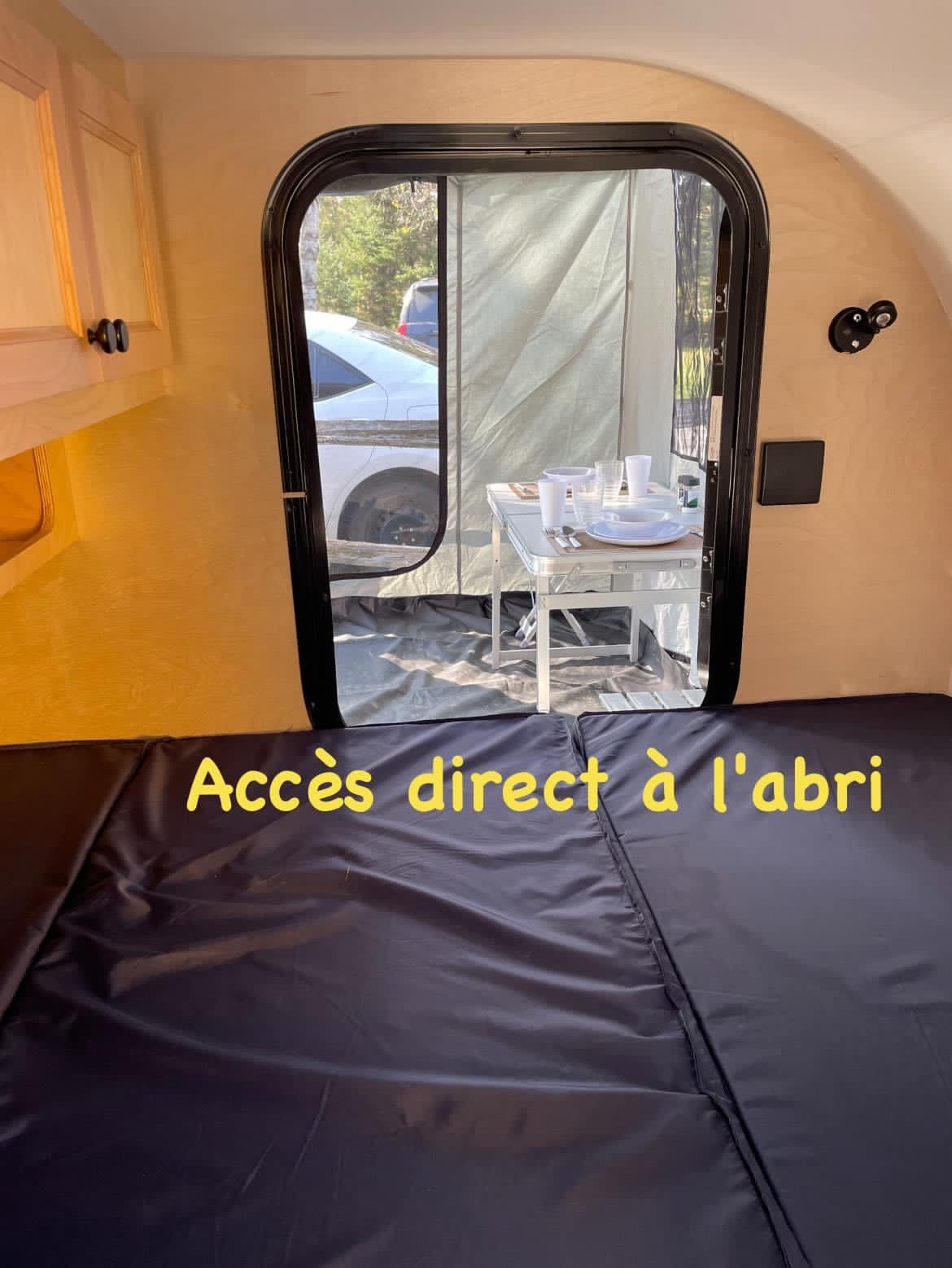 Cozy RV rental interior: comfortable bed & direct access to an outdoor dining shelter with table.. Car-gotrailers liberty2goXL 2021