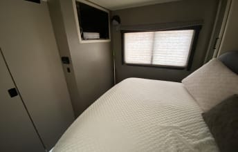 This RV rental bedroom offers a comfortable bed, window, and TV, ideal for compact travel lodging.. Thor A.C.E. 2021