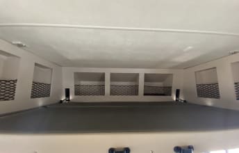 Inside an RV rental, this cozy bunk bed area features convenient overhead storage cubbies with mesh netting and reading lights.. Thor A.C.E. 2021