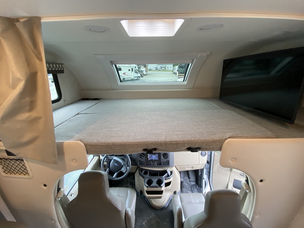 Inside an RV rental, a large cab-over bed sits above the driver's cockpit with a TV mounted on the right wall.. Thor Motor Coach Echelon LC25 2022