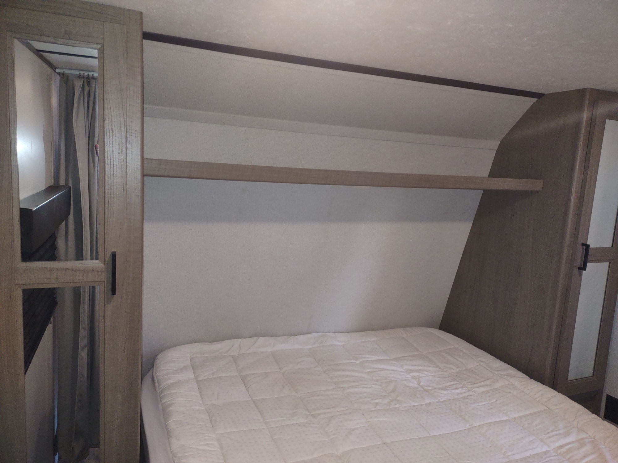 RV rental bedroom with a comfortable bed, overhead storage shelf, and mirrored wardrobes on each side.. Keystone Hideout 2020