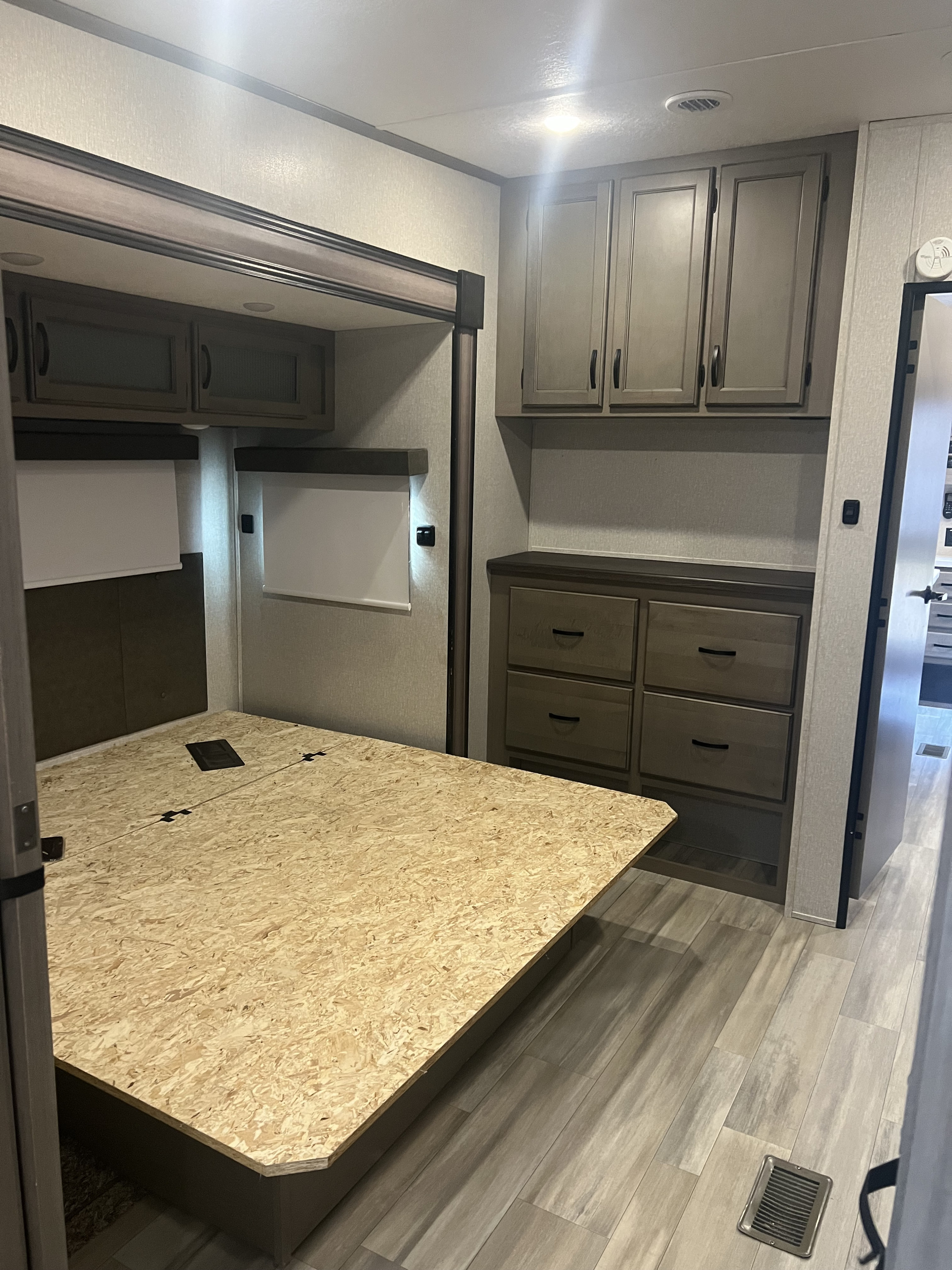 RV rental bedroom with bare OSB bed platform, built-in storage cabinets, wood-look flooring, and ceiling/cabinet lighting.. Coachmen Chaparral 2021