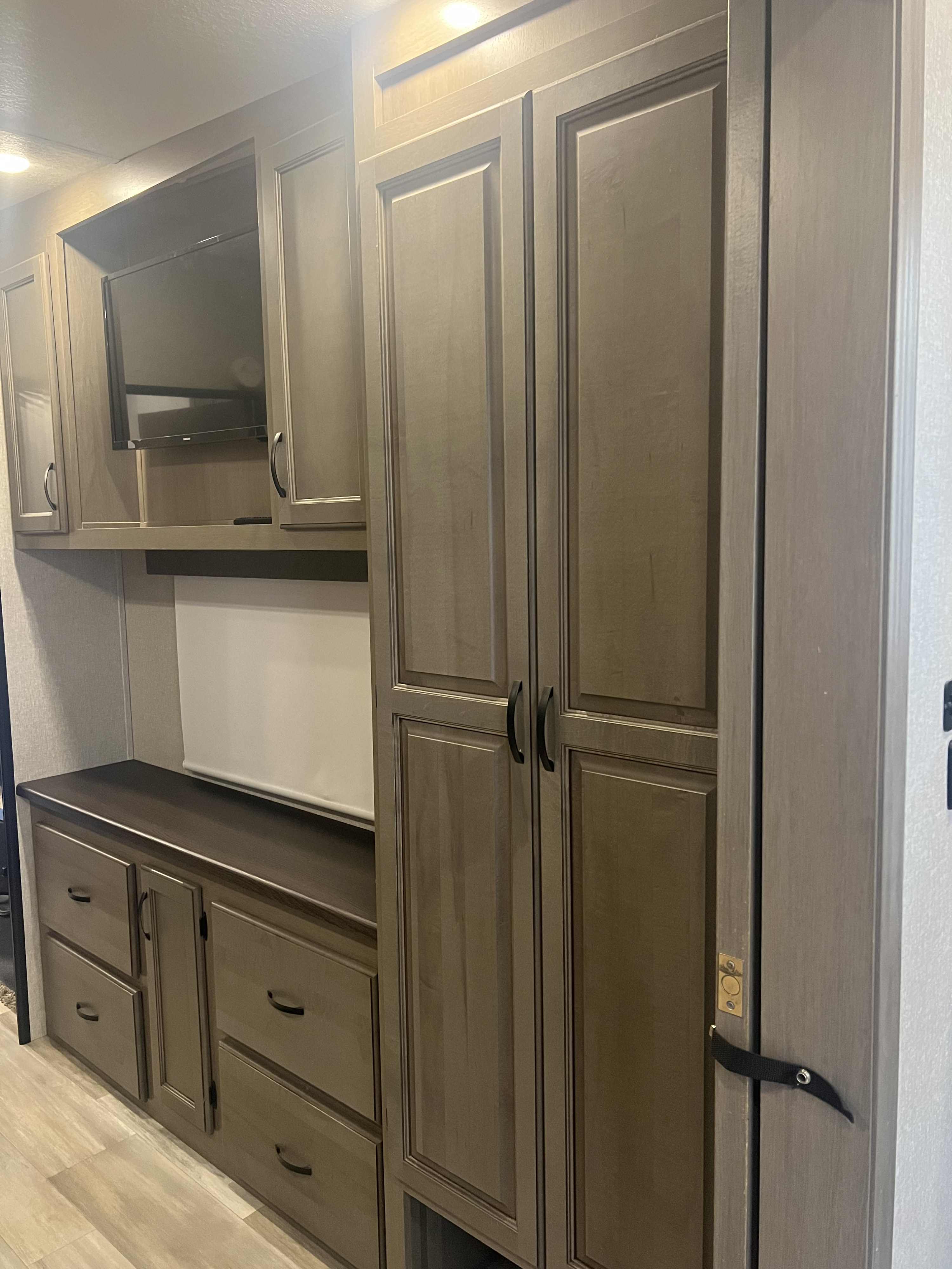 RV rental interior showing a built-in entertainment unit with a TV, upper cabinets, lower drawers, and a tall wardrobe.. Coachmen Chaparral 2021