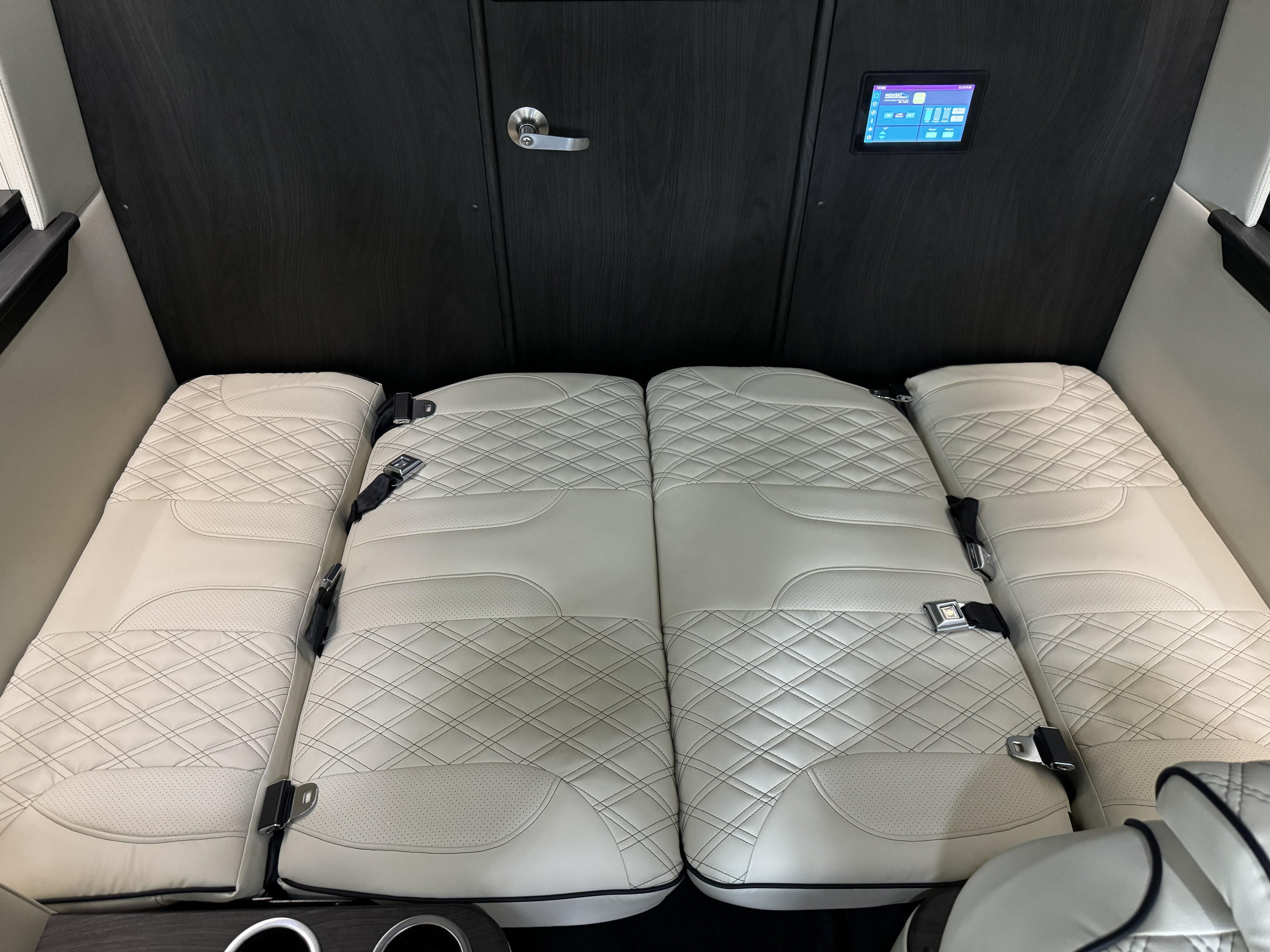 The cozy interior of an RV rental, featuring white quilted convertible seats, seatbelts, and a digital control panel.. Midwest Automotive Designs Day Cruiser 2023