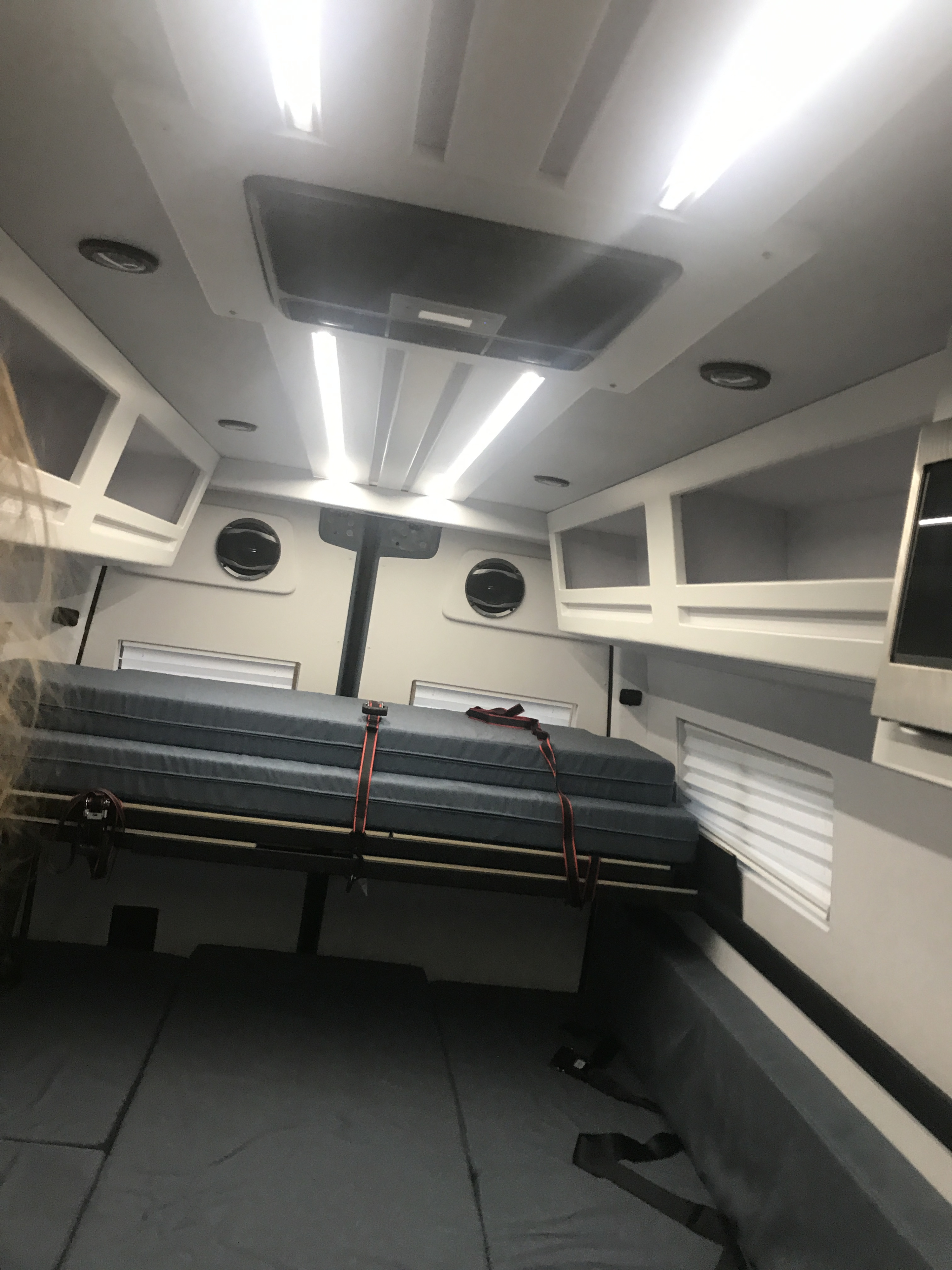 Inside an RV rental, a compact sleeping area with a secure bunk bed, lower mattress, bright lights, and cabinets for efficient travel.. Mercedes-Benz Sprinter 2022