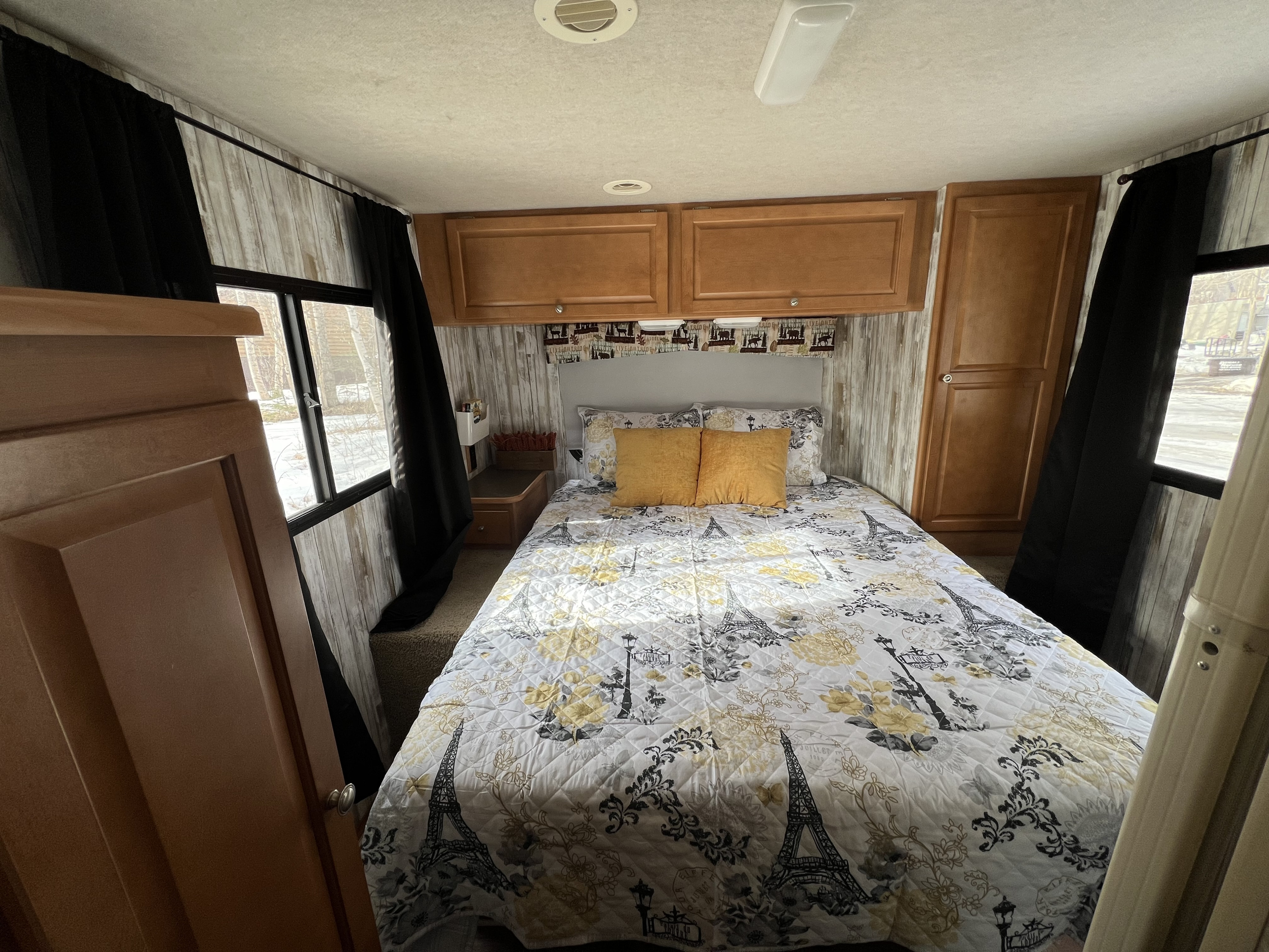 Cozy RV rental bedroom featuring Paris-themed bedding, wood cabinets, and natural light.. Winnebago Chalet 2010