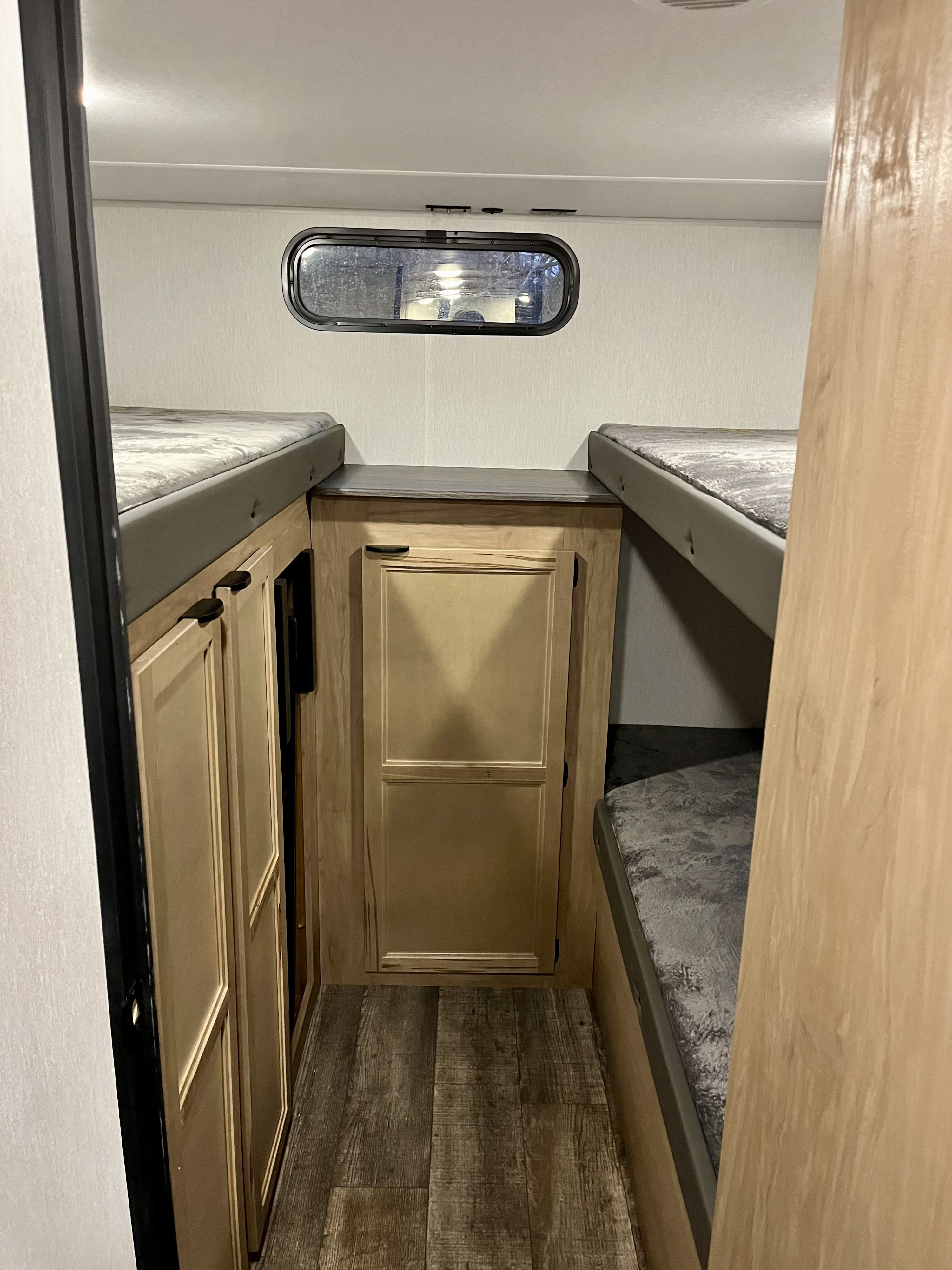 RV rental interior: bunk beds flanking a central cabinet with countertop & window, maximizing space.. Forest River Grey Wolf 29TE 2024