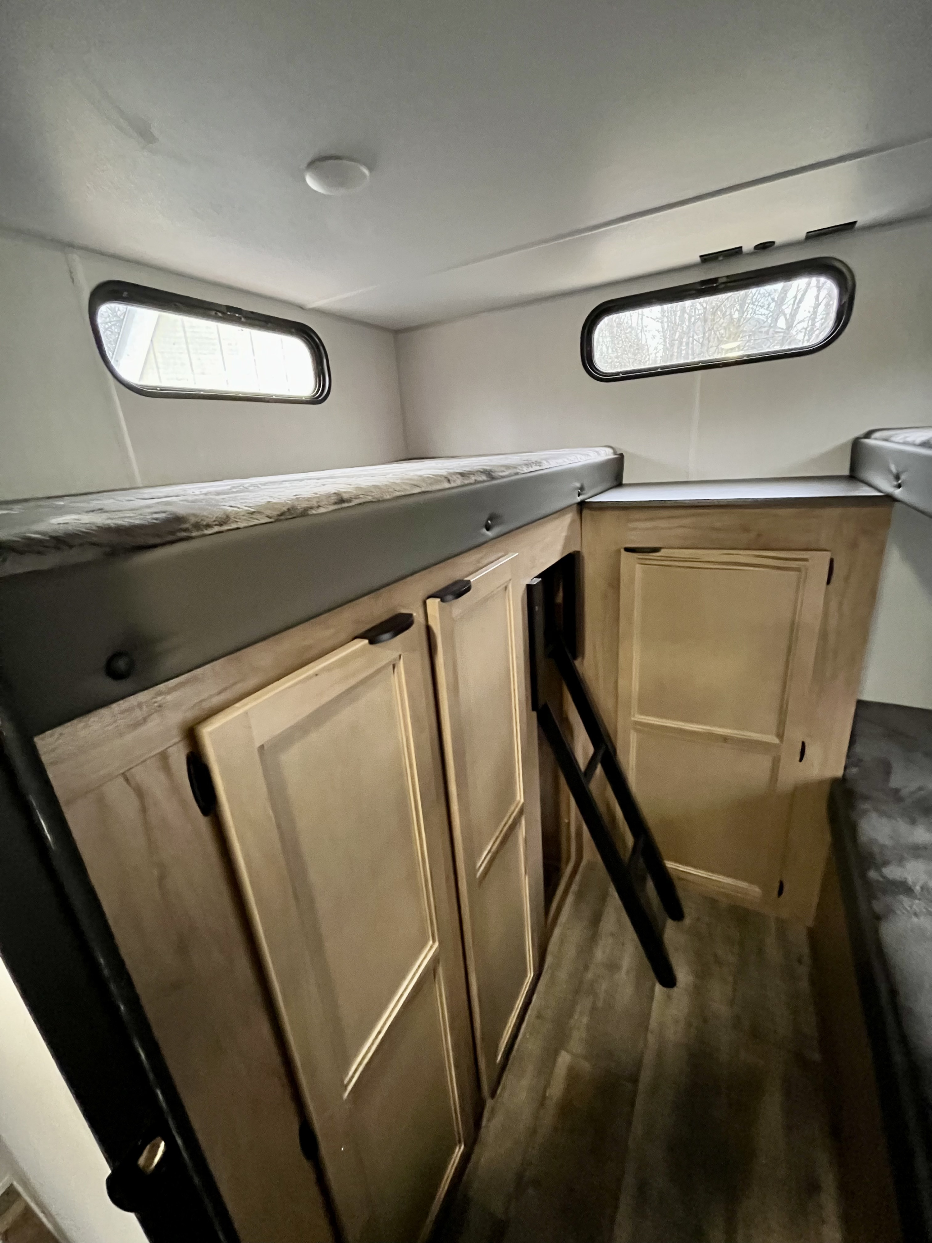 Interior of an RV rental: bunk beds with built-in storage cabinets, a ladder, and small windows, offering practical sleep space.. Forest River Grey Wolf 29TE 2024