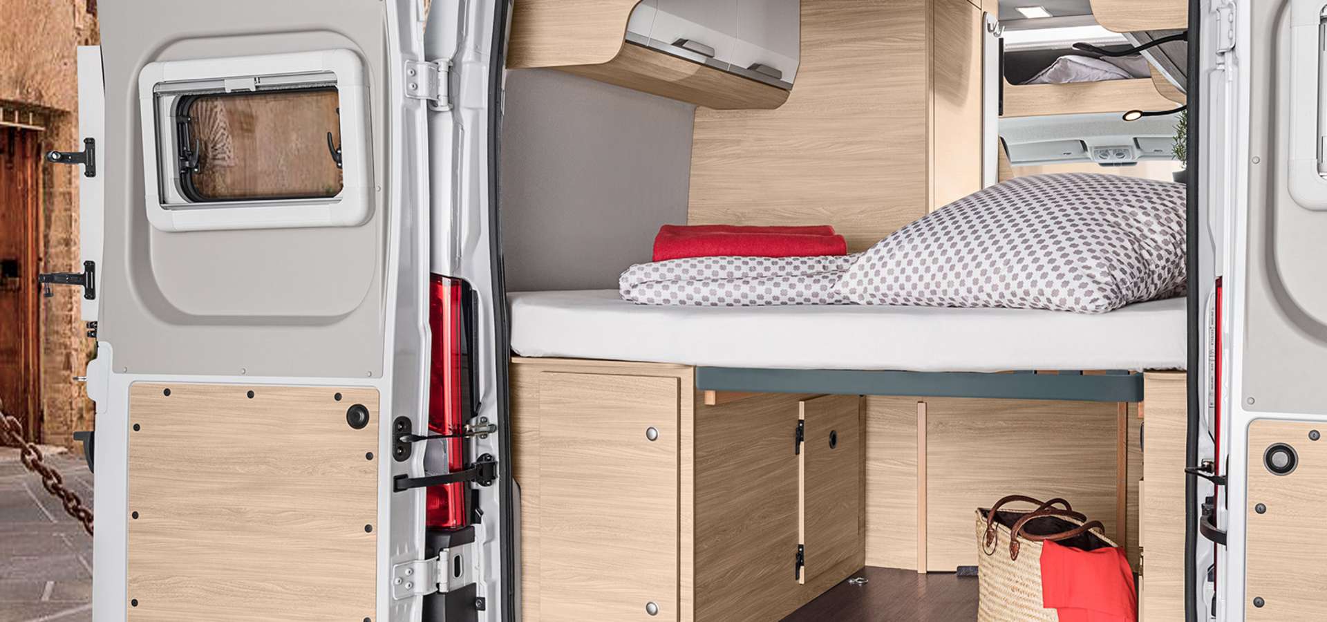 This cozy RV rental interior features a comfortable bed, smart storage, and an open rear door revealing the exterior.. Knaus Boxstar 540mq 2024